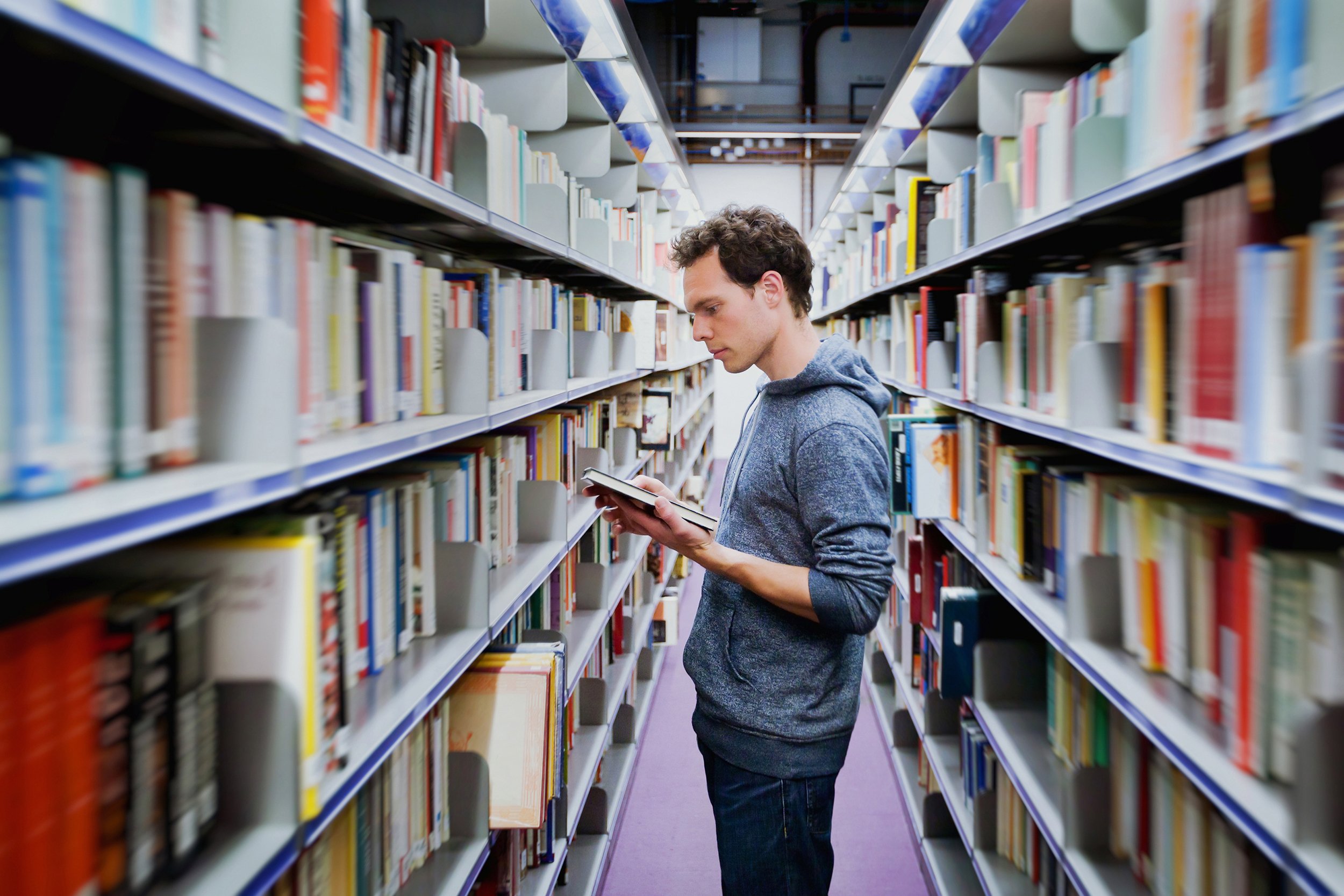 student reading book between the shelves in the library
