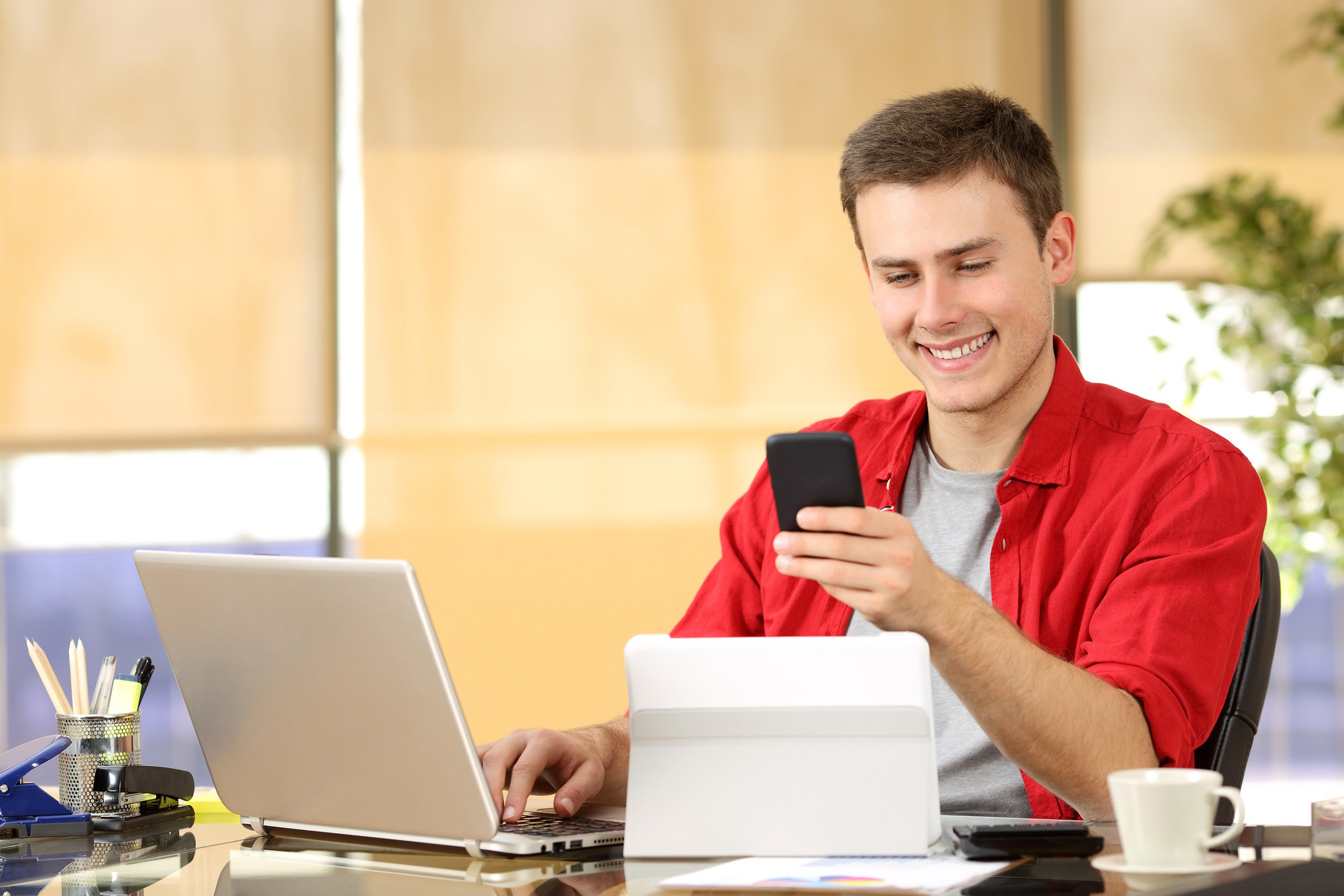 Young man in a red shirt reading an email at work