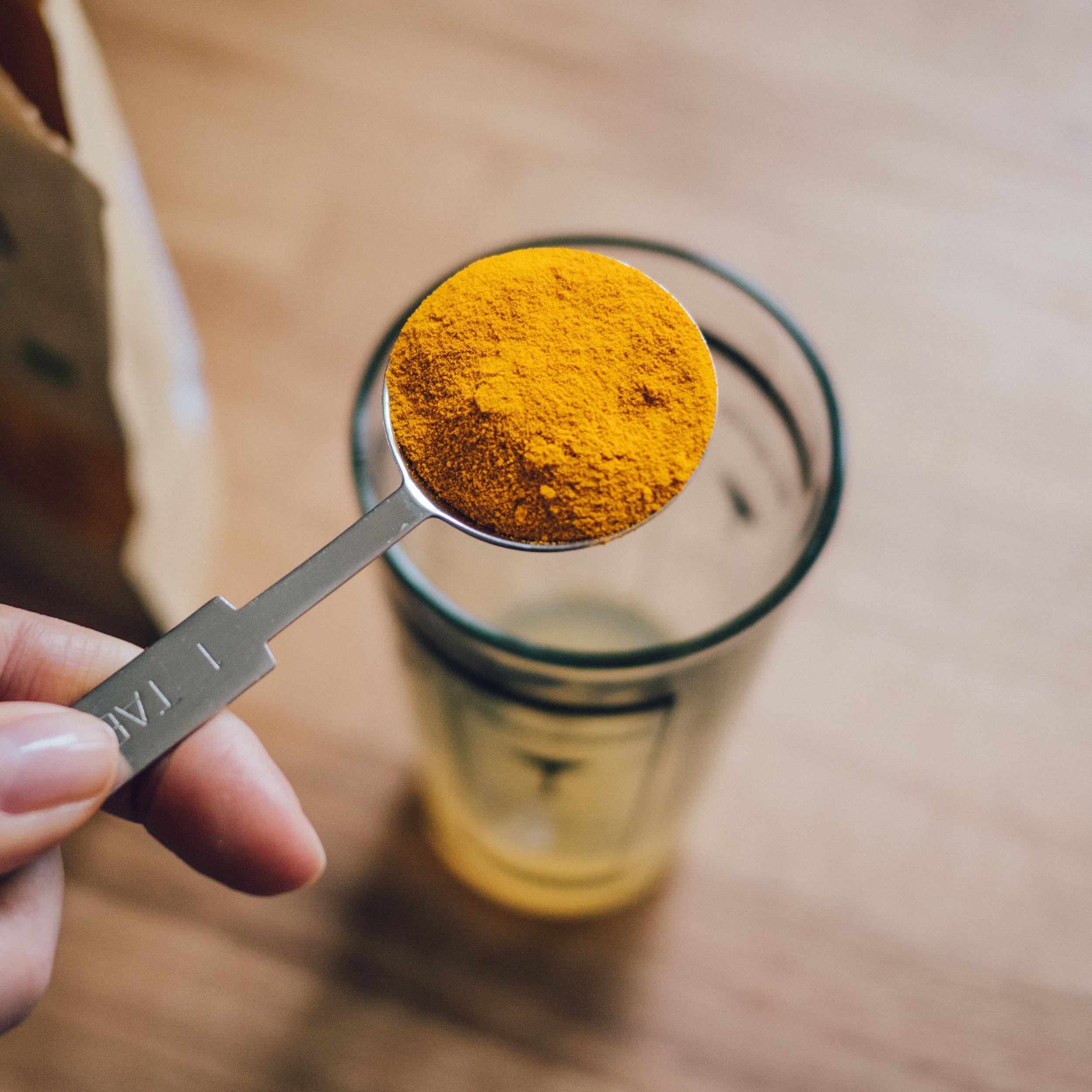 turmeric powder in spoon about to be poured in glass