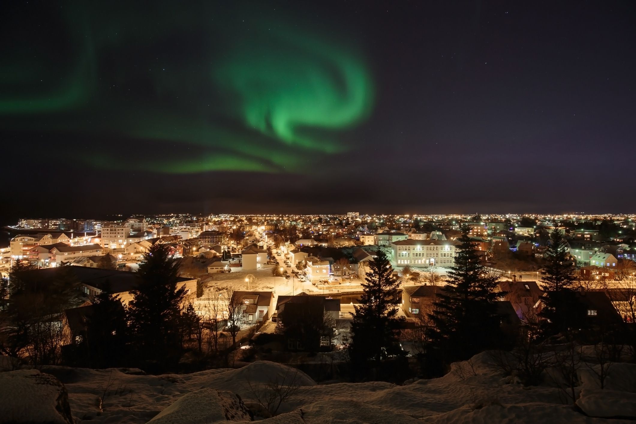 Auroras blazing in the sky above the Reykjavik area in Iceland around christmas time, snow on the ground.