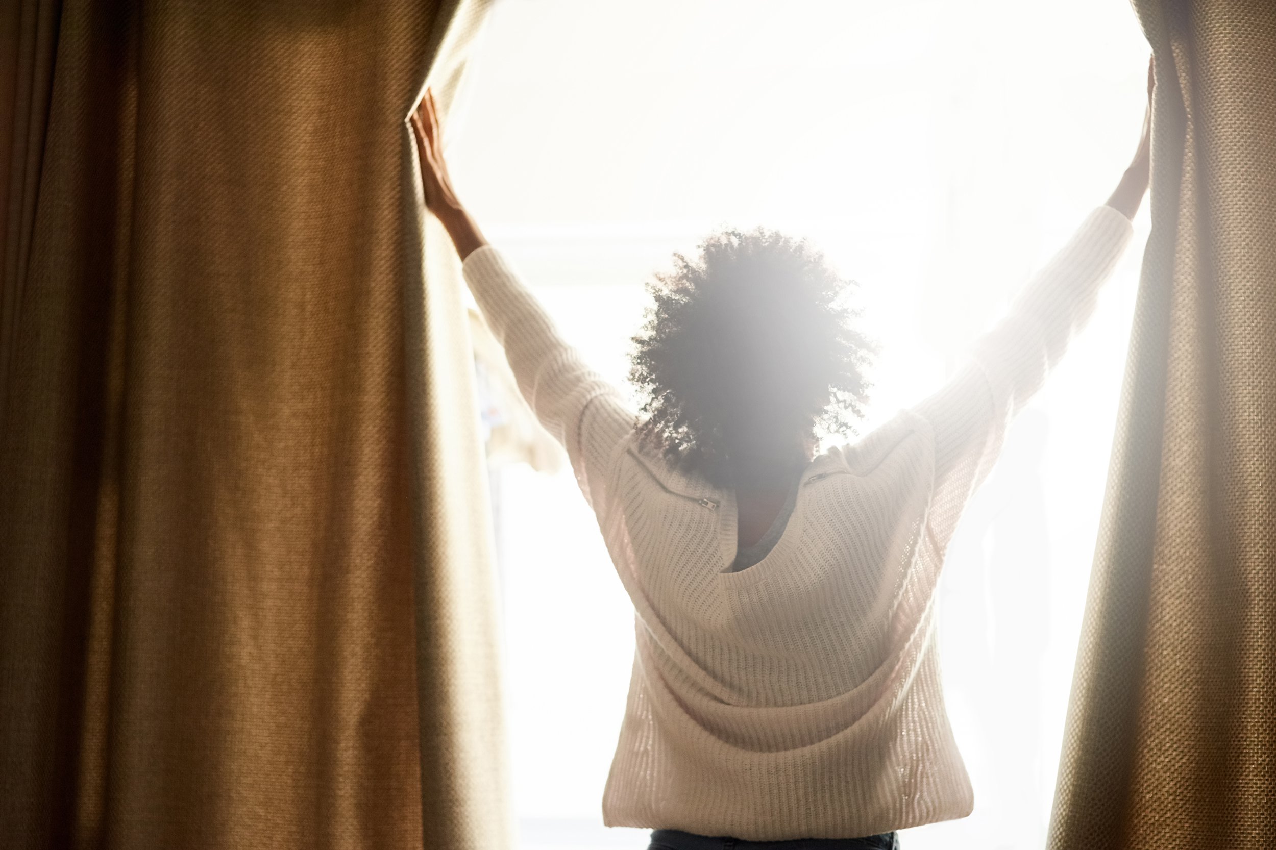 African American woman opening window, letting the light in