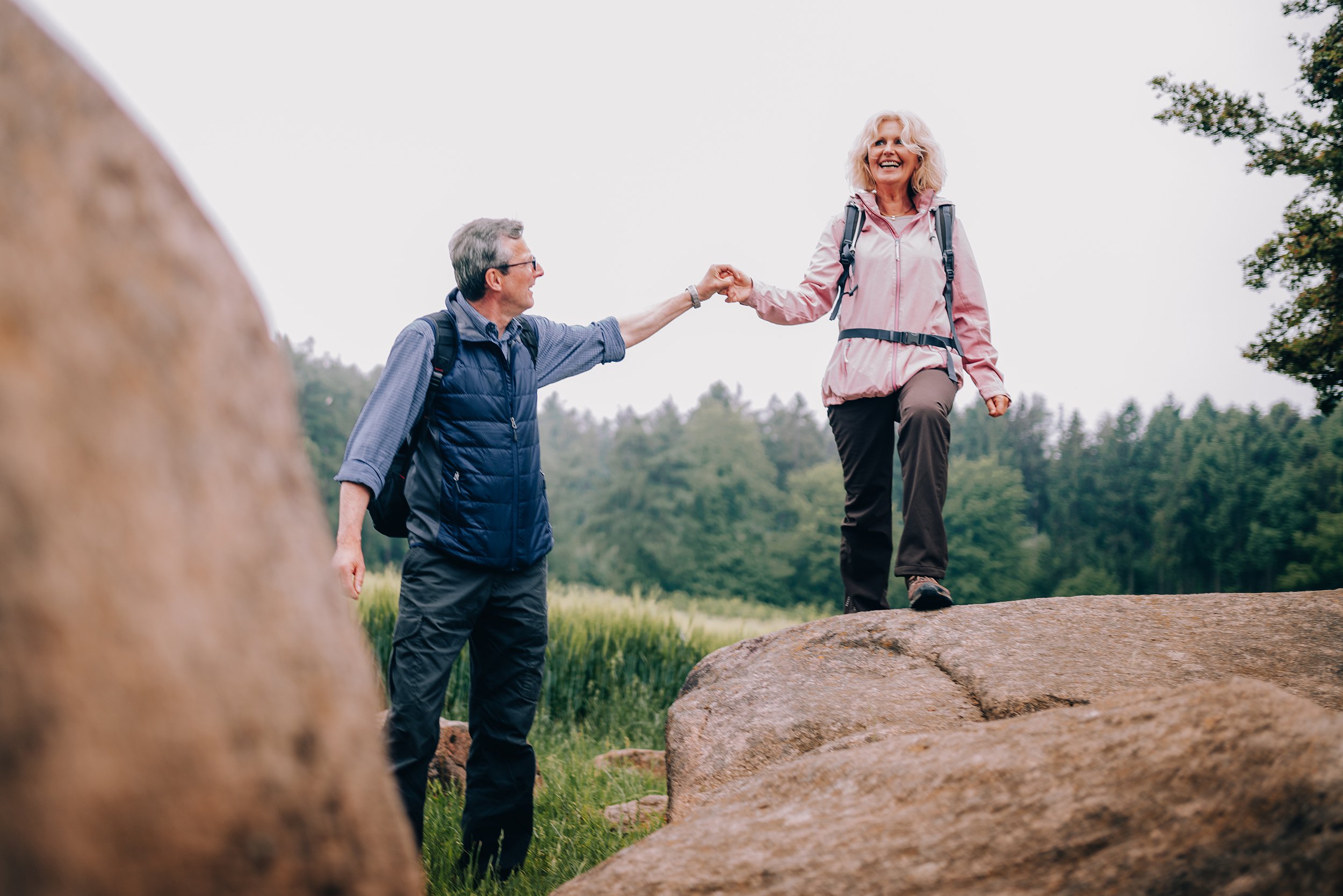 senior man helping his wife climbing up a rock on