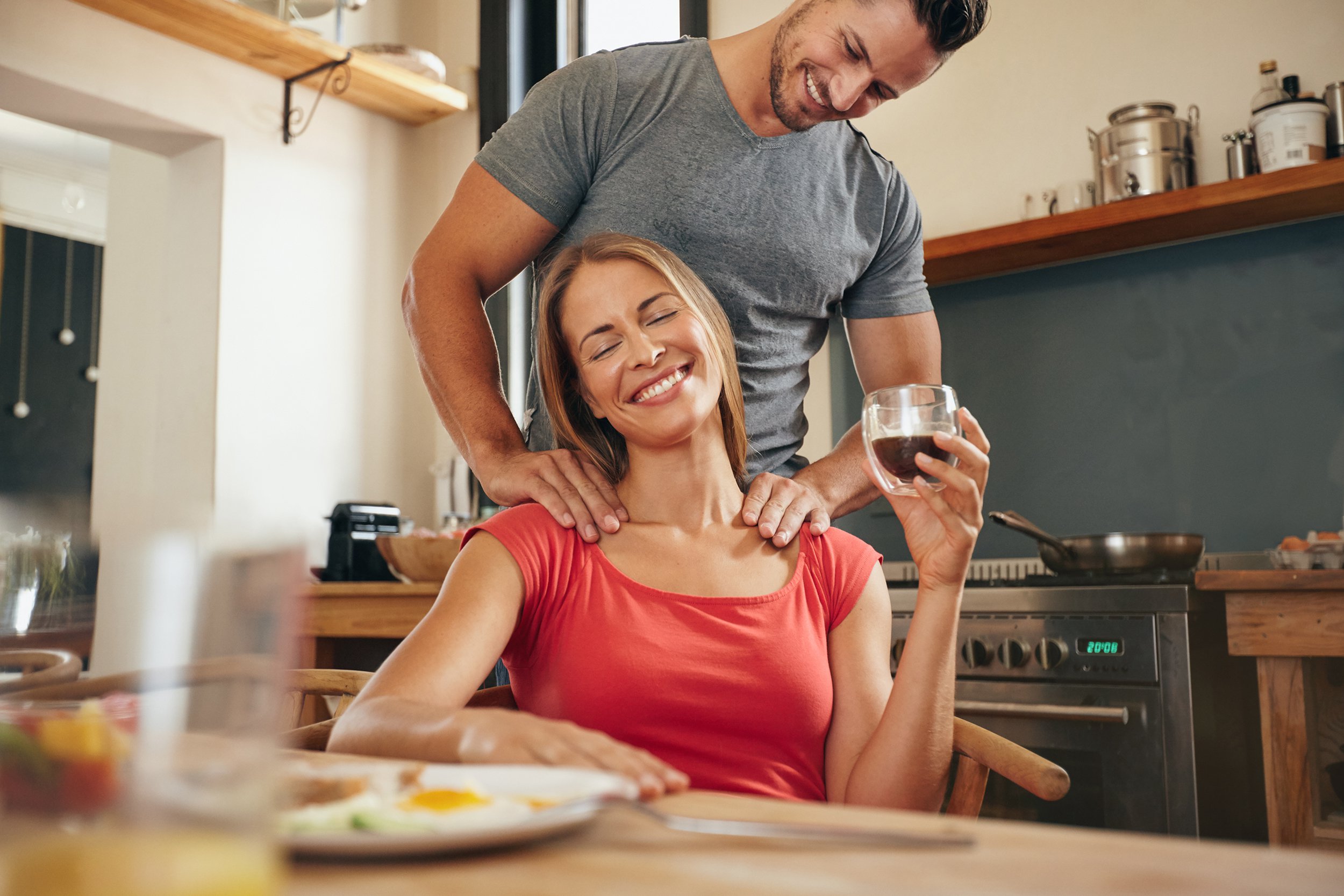 woman relaxing while man massaging her shoulders in kitchen