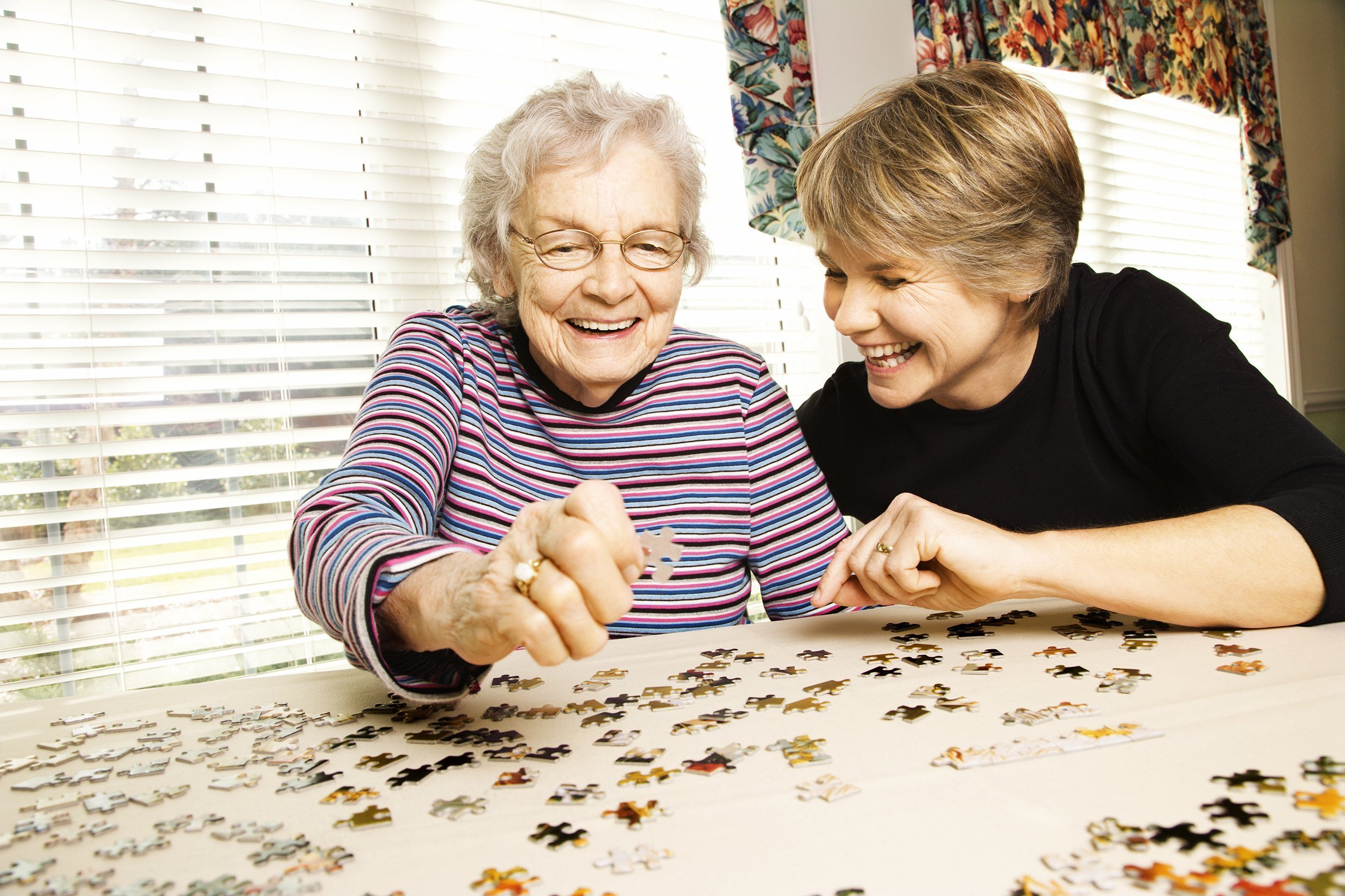elderly woman and a younger woman work on a jigsaw puzzle