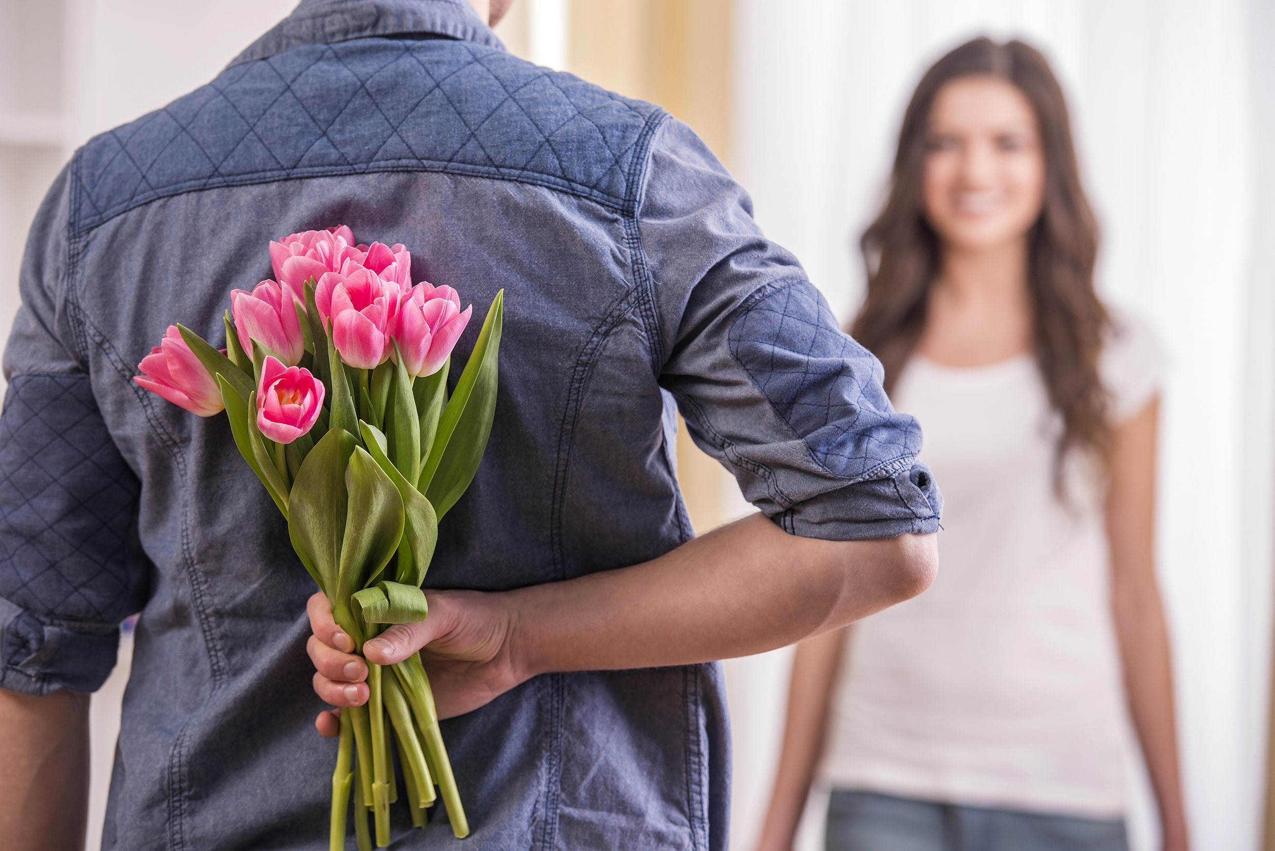 man is hiding flowers behind their backs to his wife at home