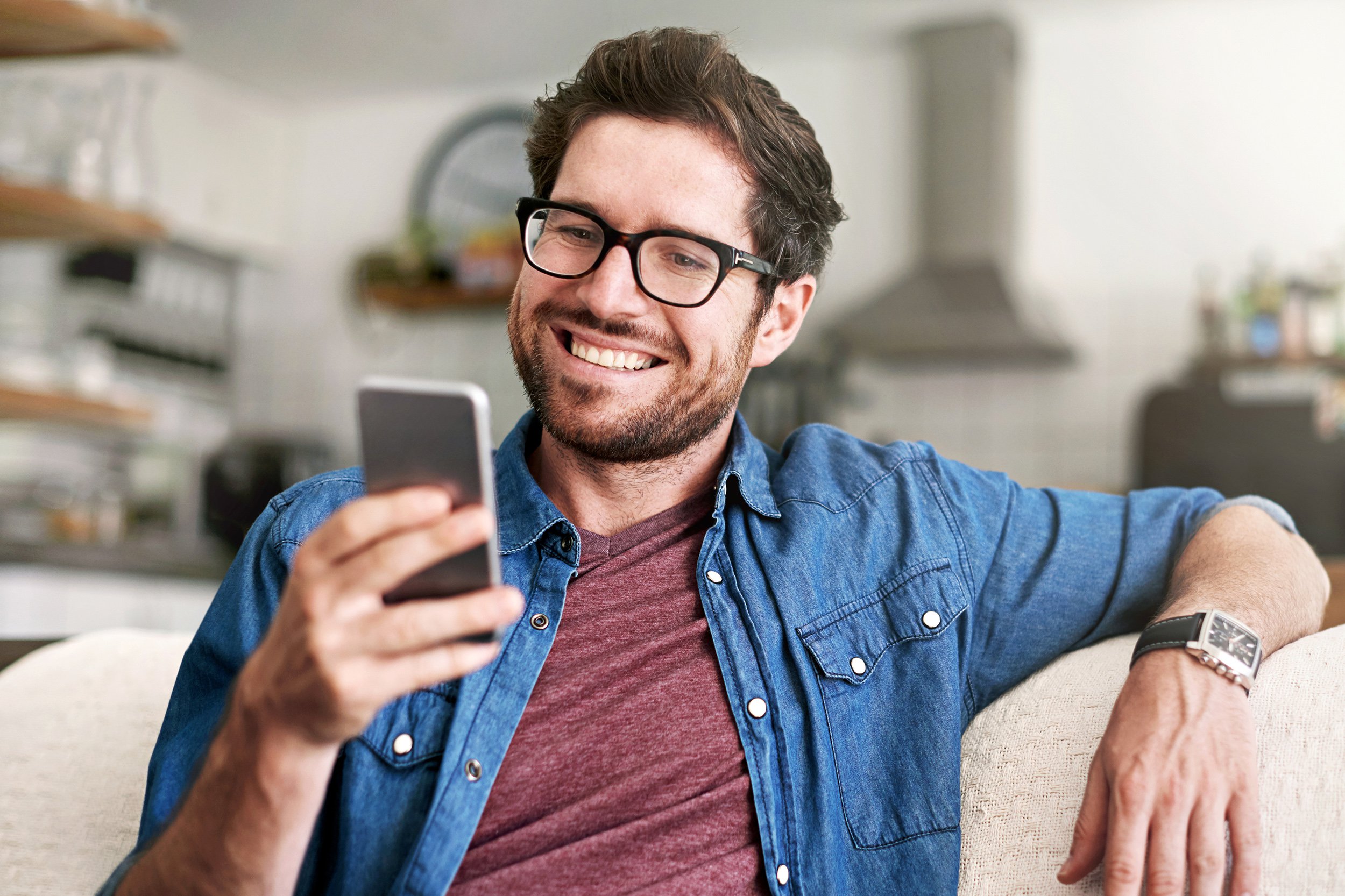 Happy man on couch at home using smartphone