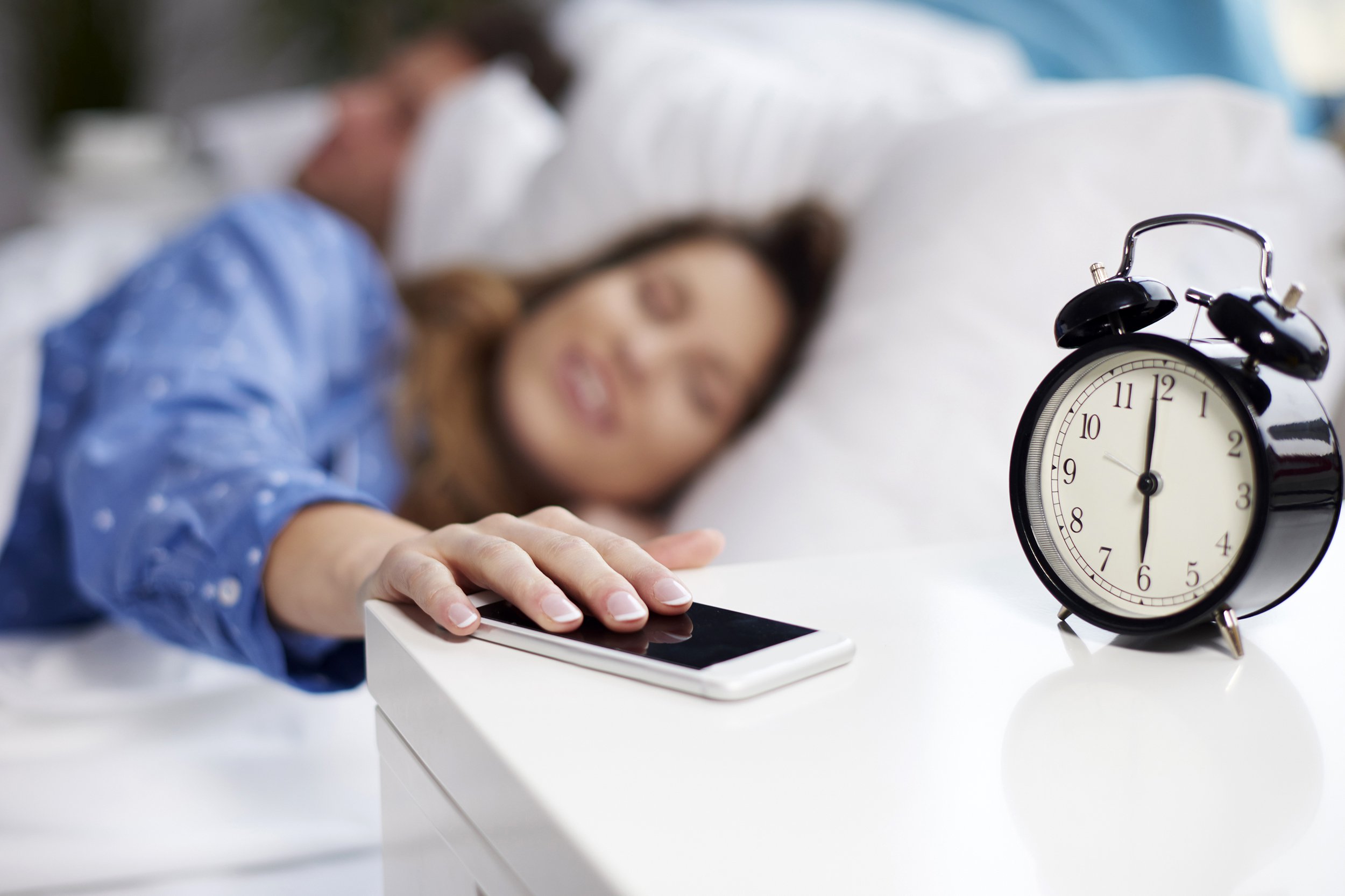 Woman waking up in bed and reaching for phone on nightstand