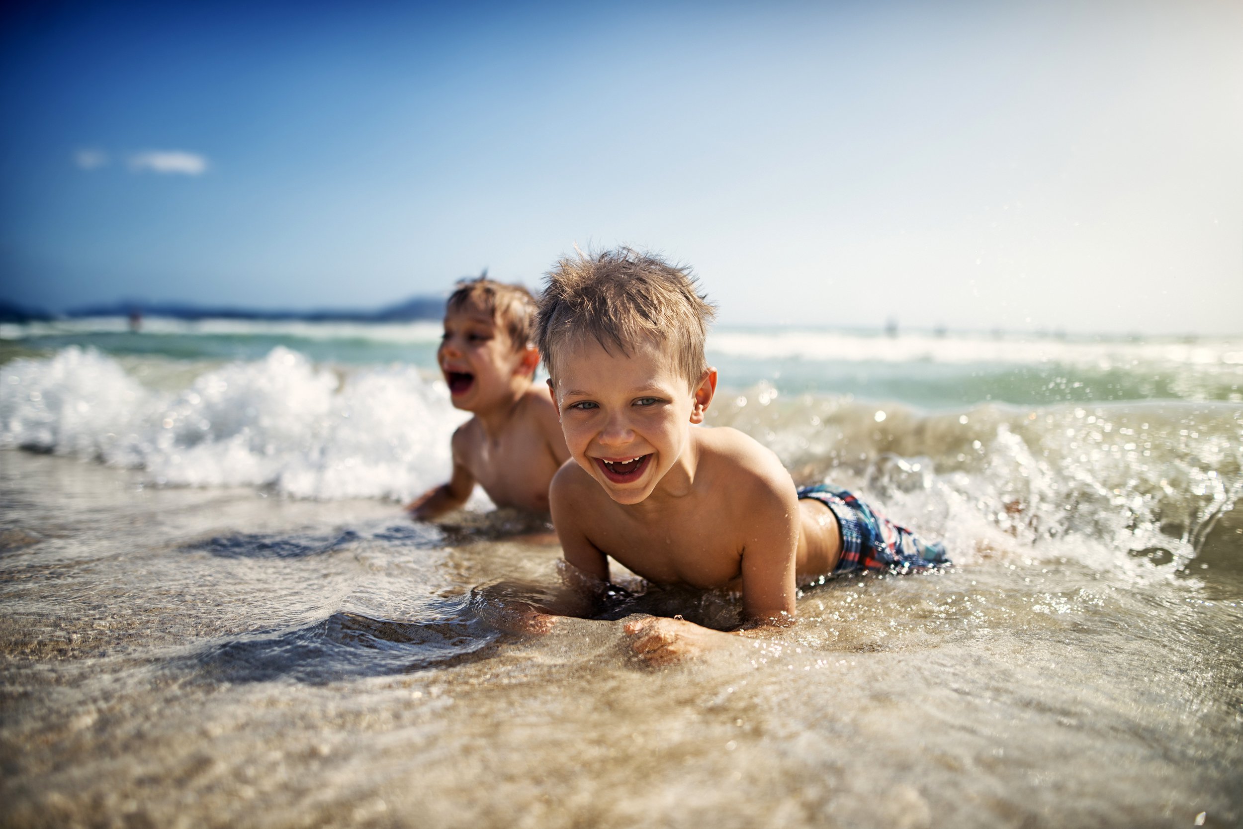 Young boys playing in the ocean, smiling at the camera