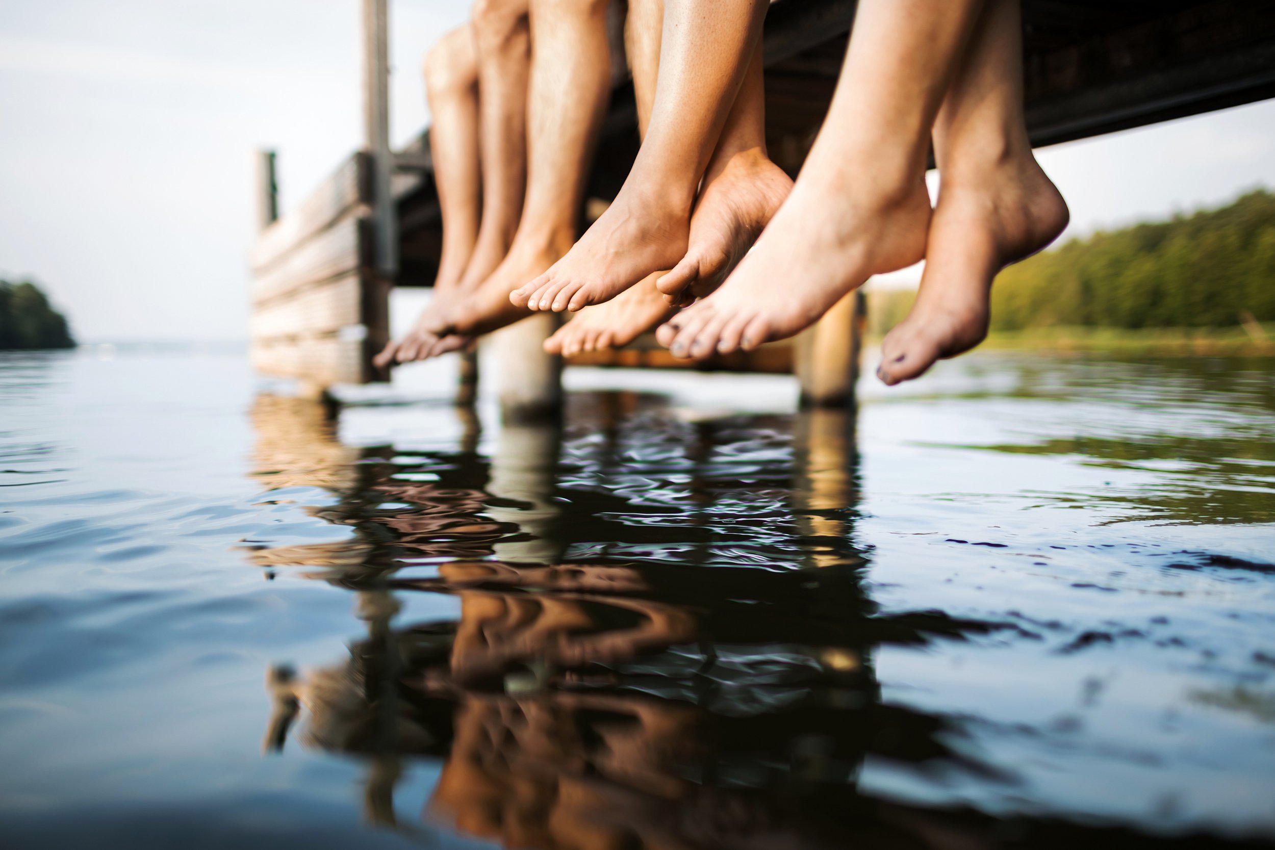 Photo of feet dangling off a dock and reflection in the lake