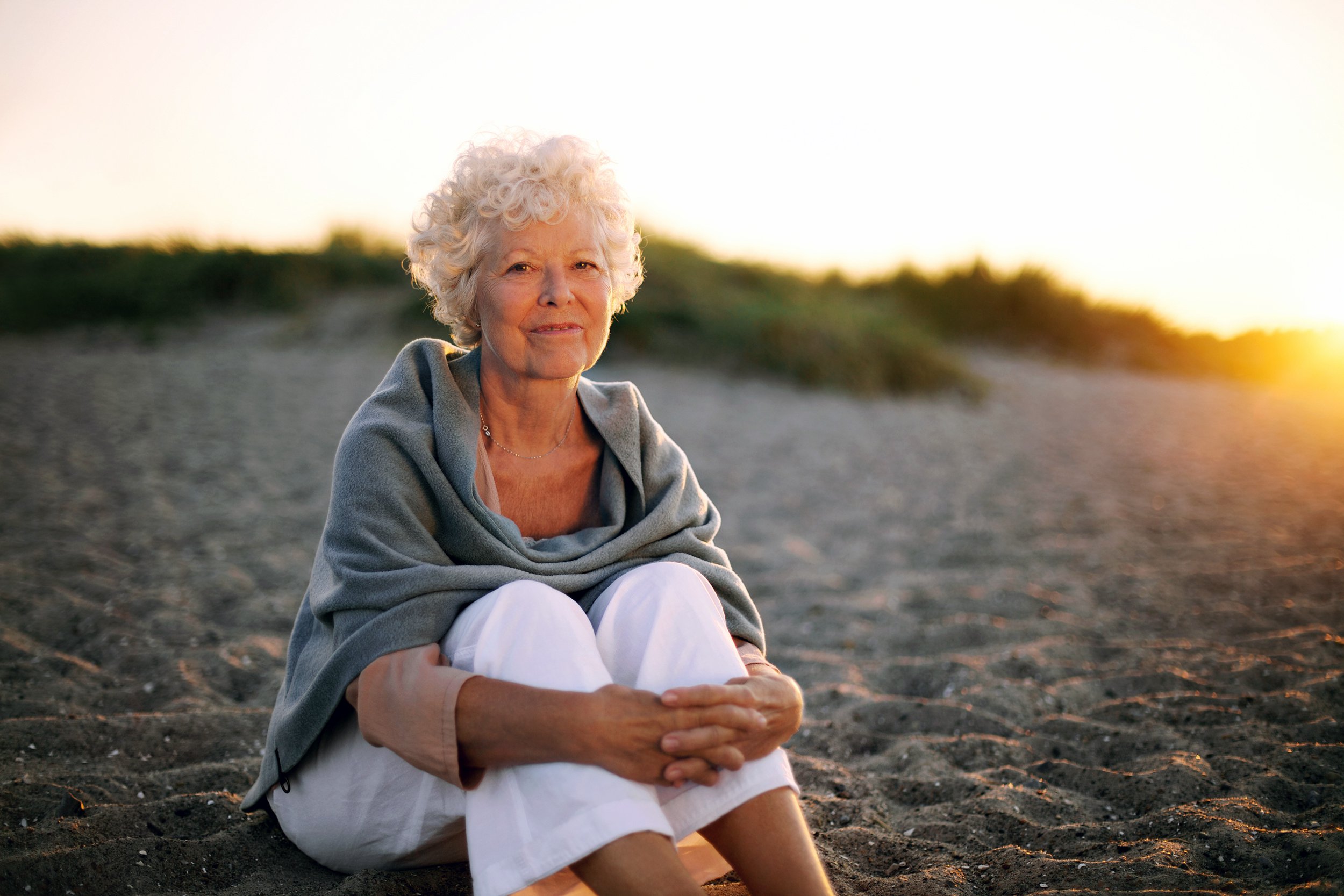 Older woman sitting on the beach at dusk