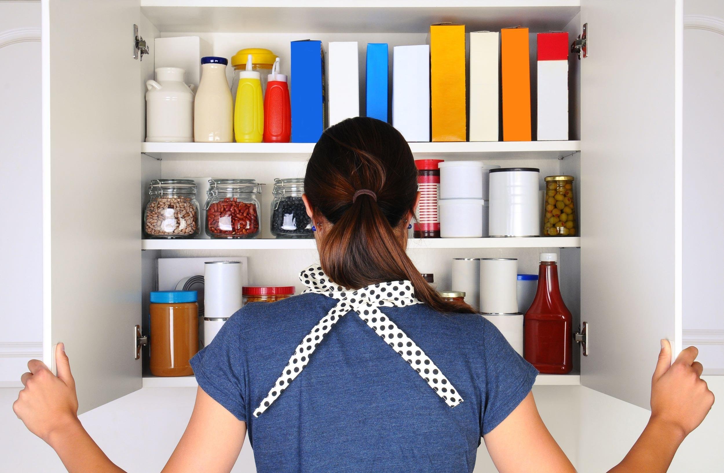 woman seen from behind opening the doors to a fully stocked pantry