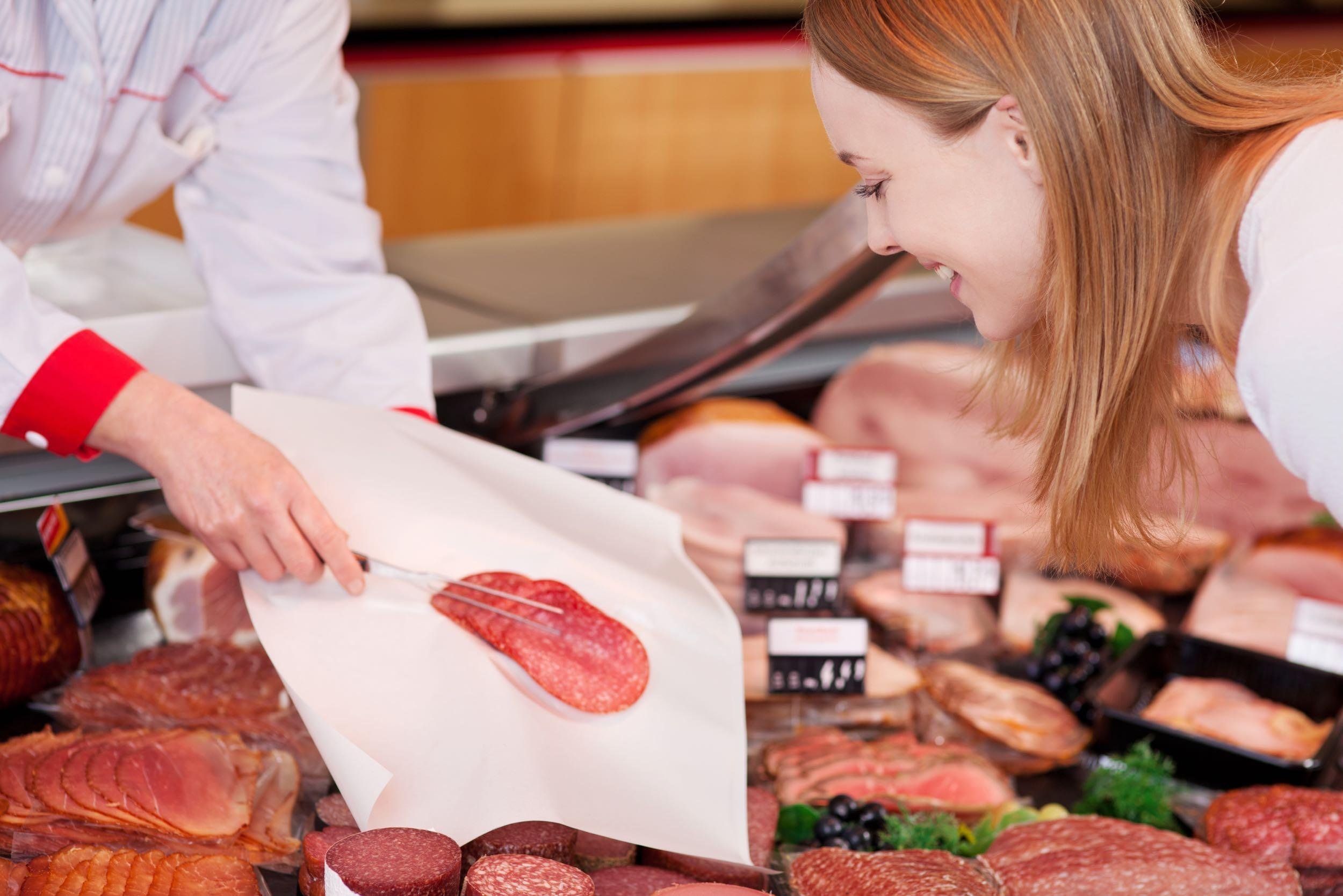 saleslady serving sliced salami on a sheet of tissue paper with a fork for a discerning female shopper