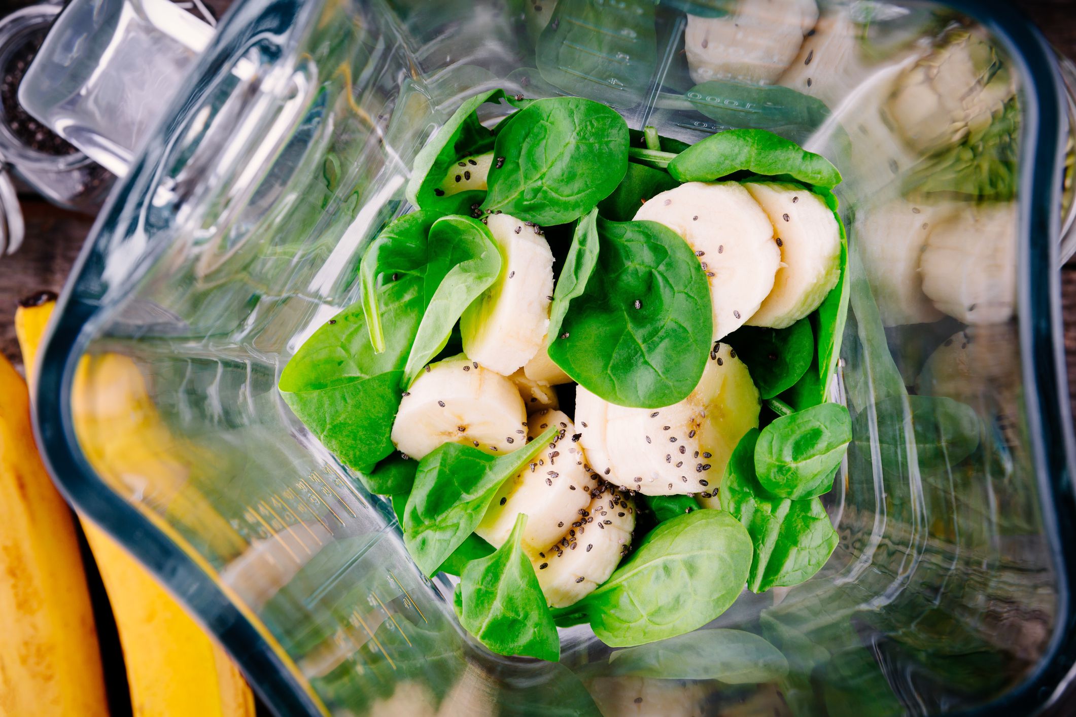 ingredients for green detox smoothies in a blender: spinach, bananas, chia seeds