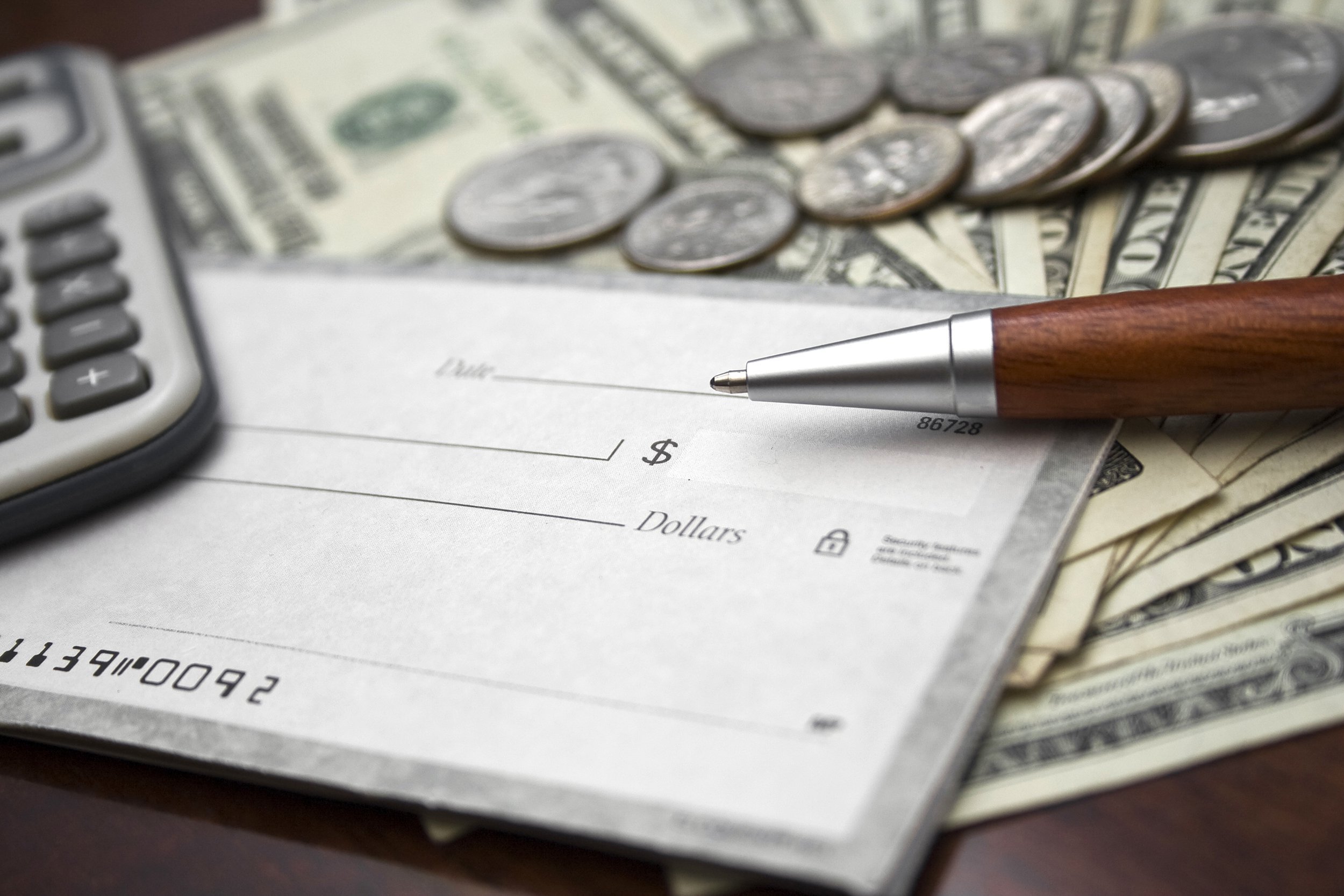 Checkbook on top of money with a pen and calculator