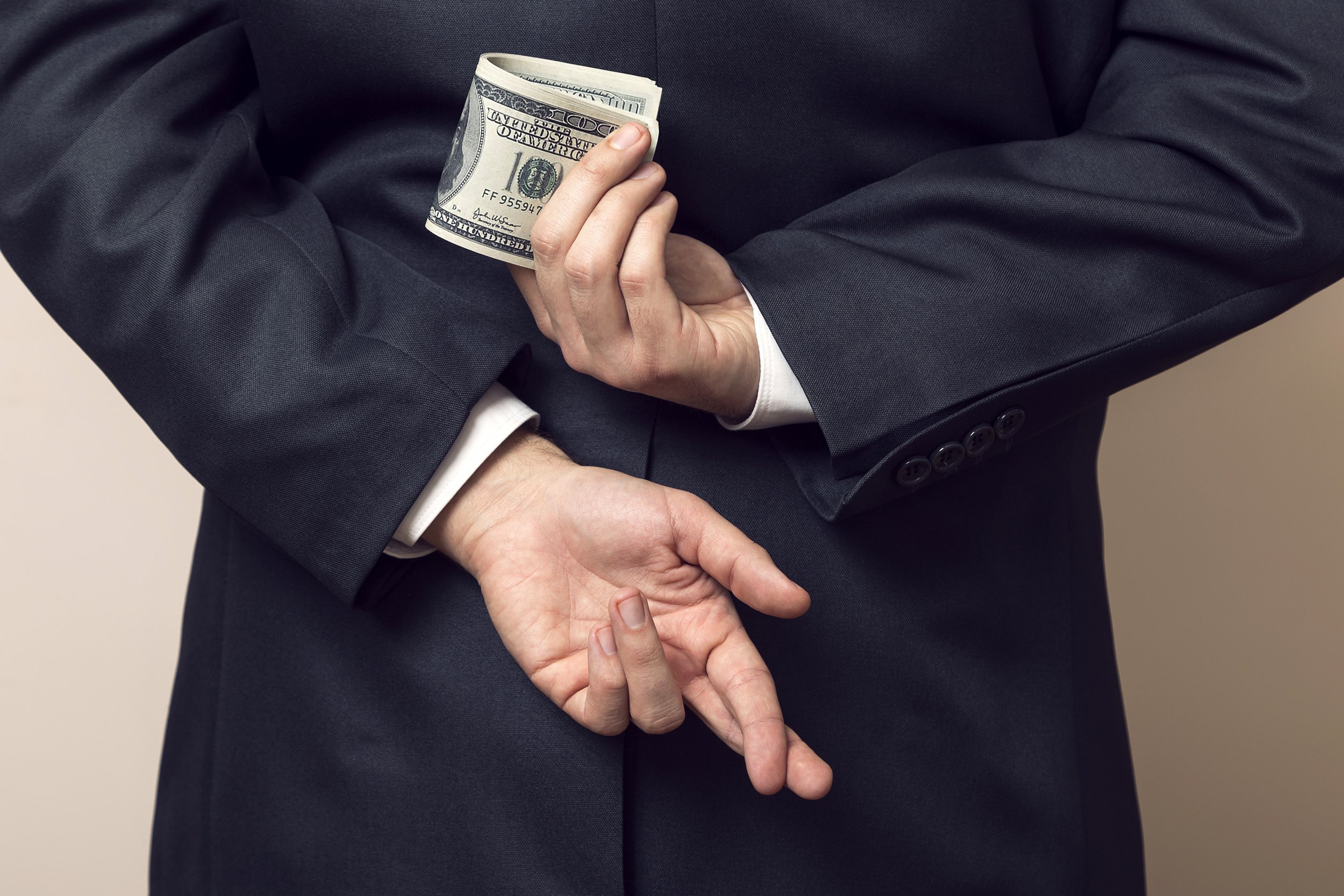 Businessman with fingers crossed behind his back and holding money