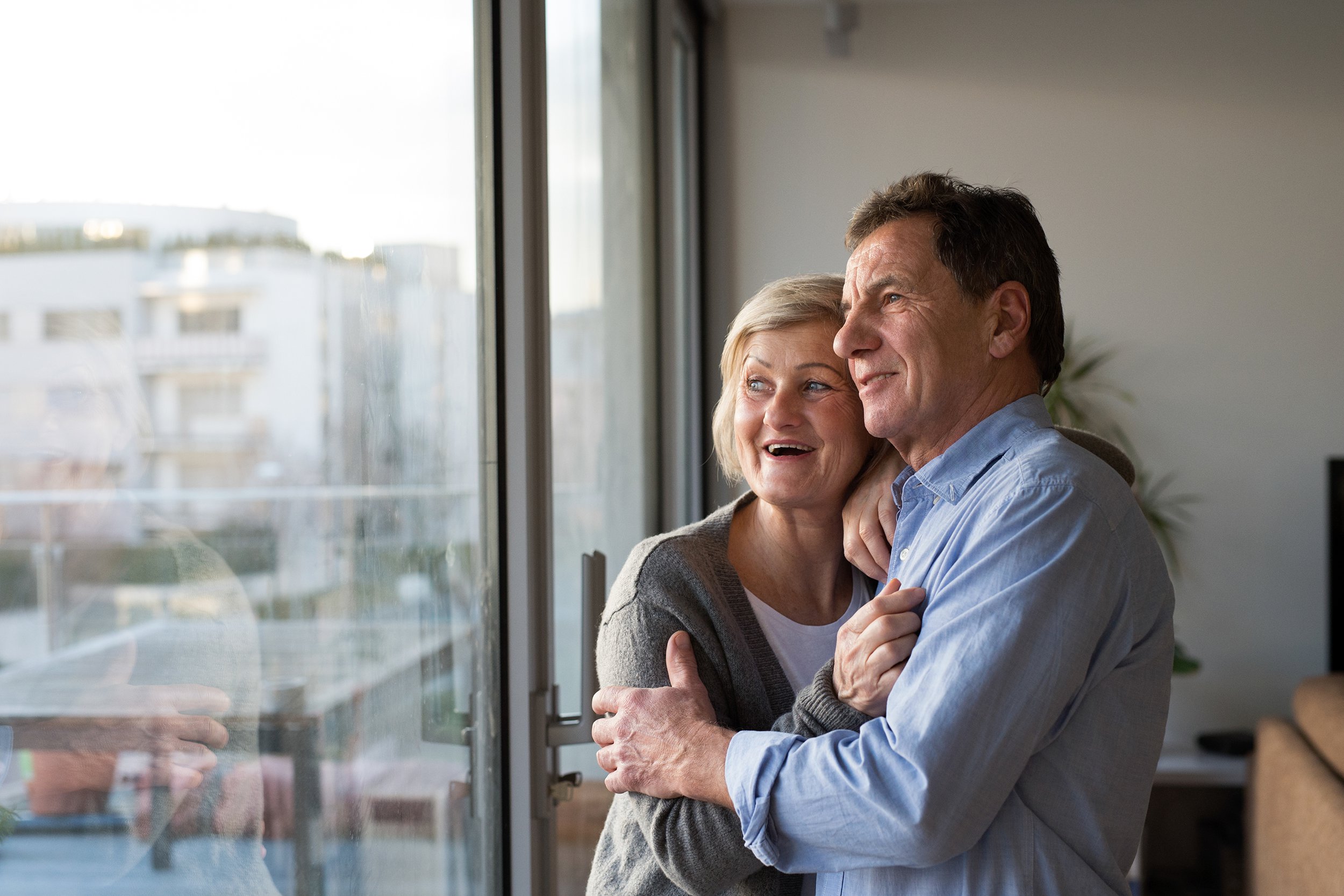 Senior couple looking out of the window in their city apartment