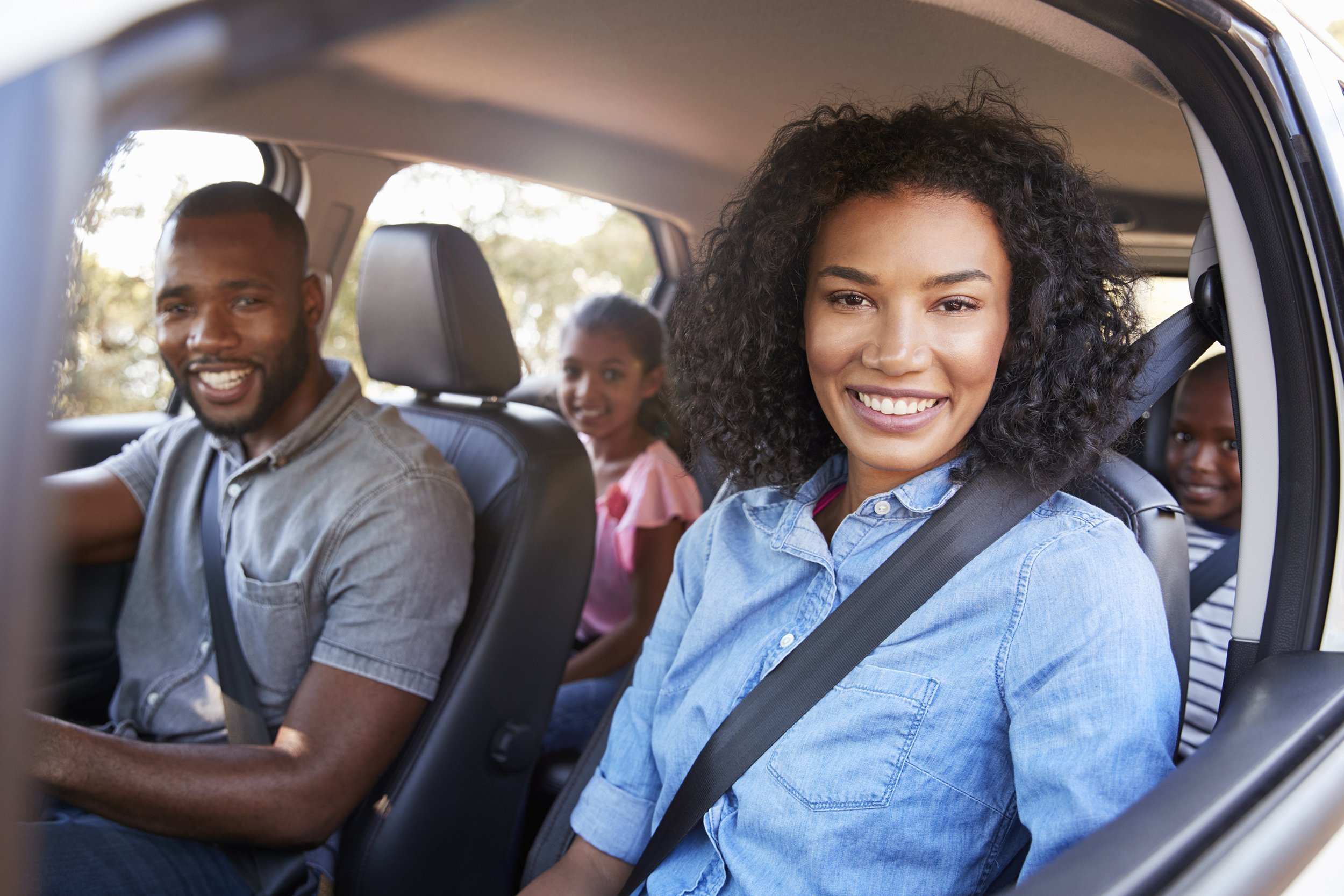 young African American family in a car on a road trip smiling to camera
