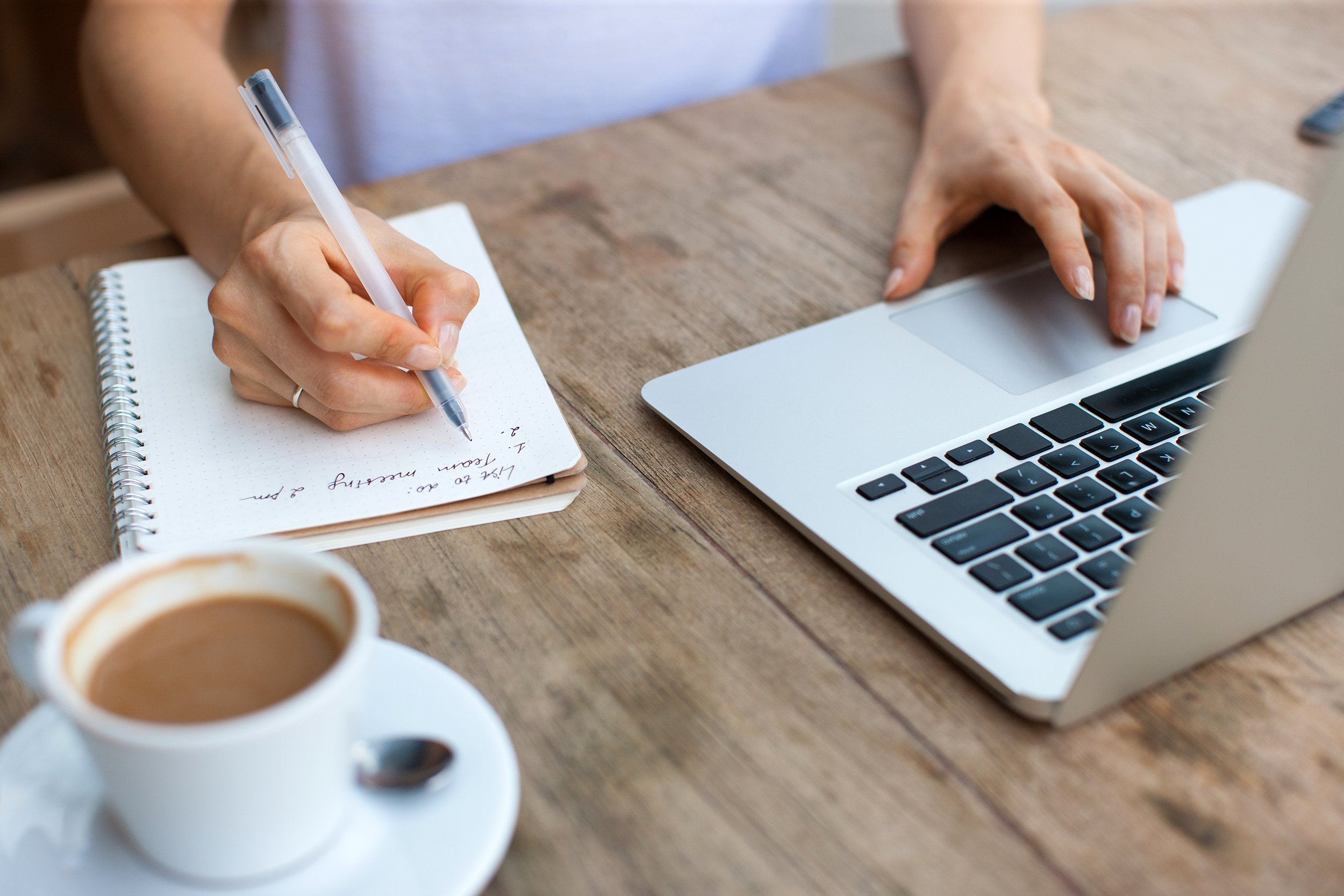 Making a list next to a laptop and a cup of coffee