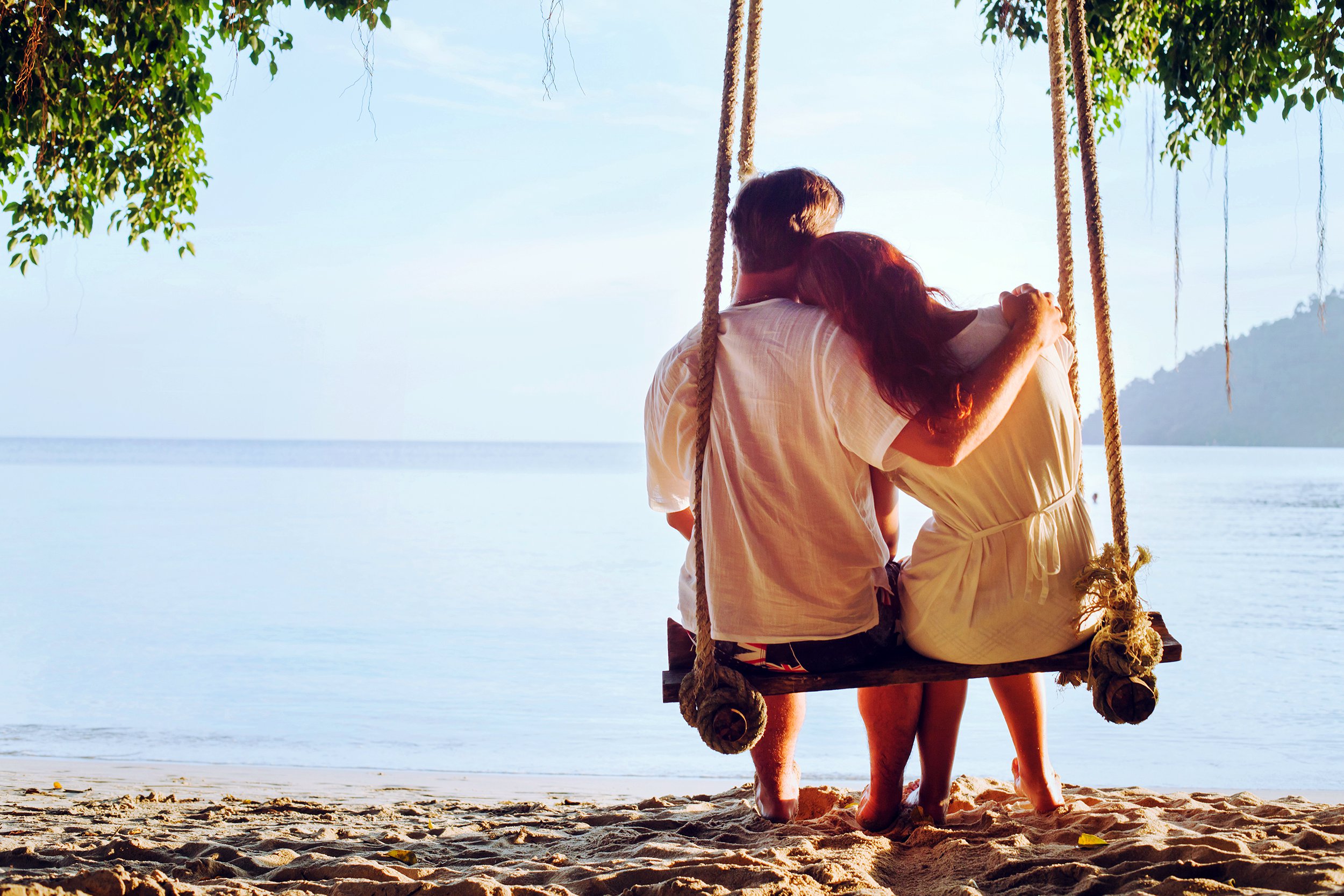 Couple sitting alone on a swinging bench near the beach