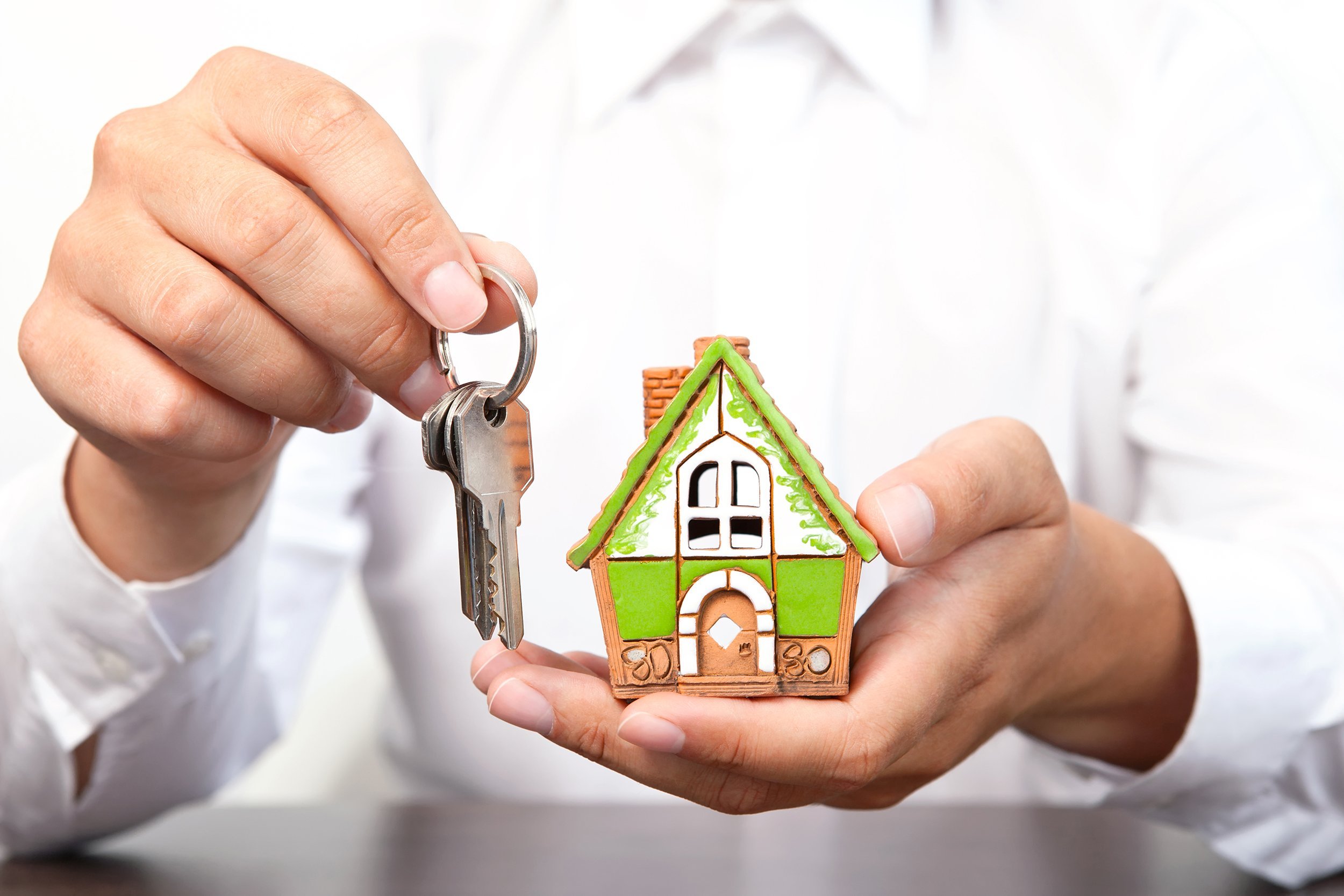 businessman in white shirt holding a small house and apartment keys in hand