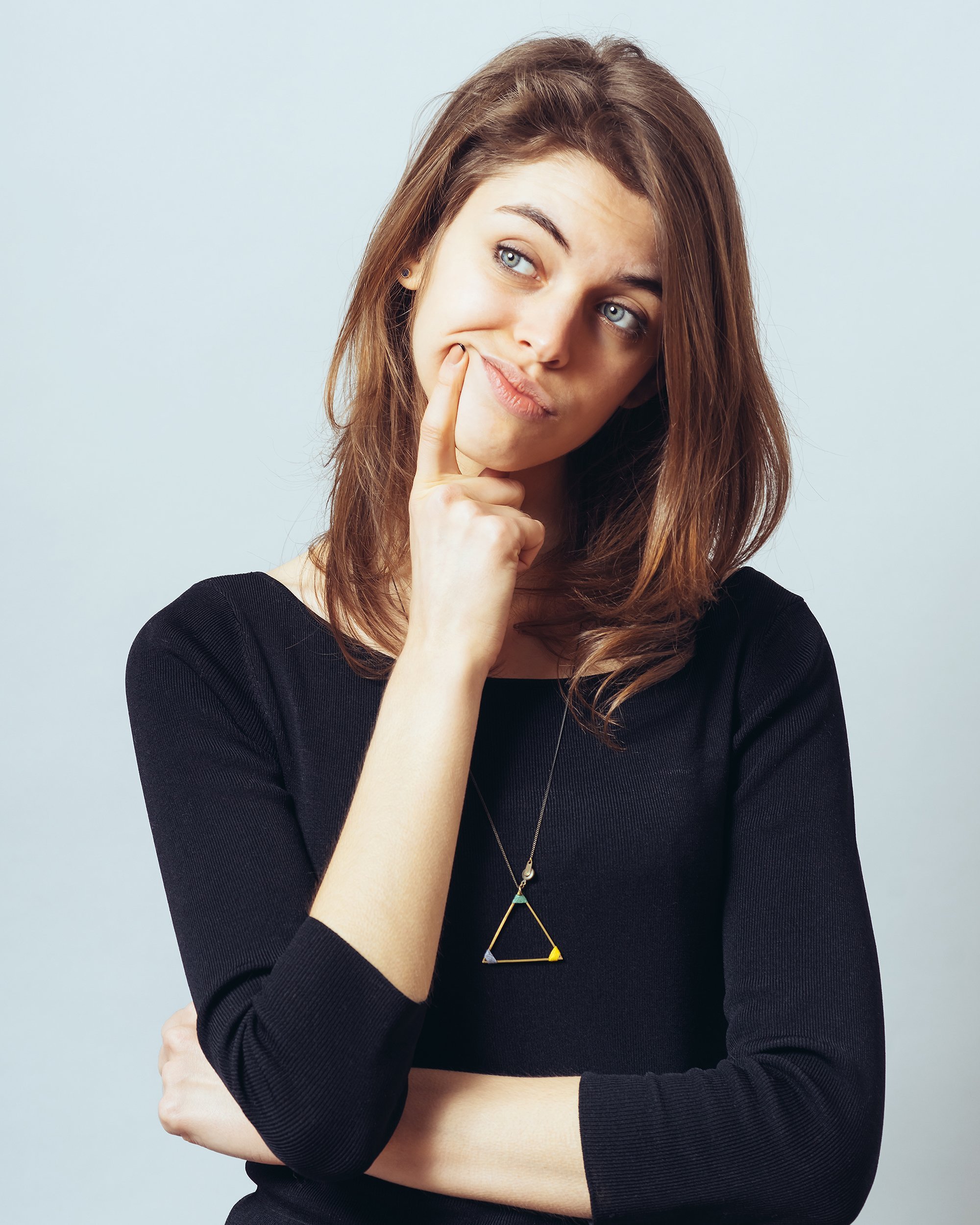 young woman has brought forefinger to mouth and looking up