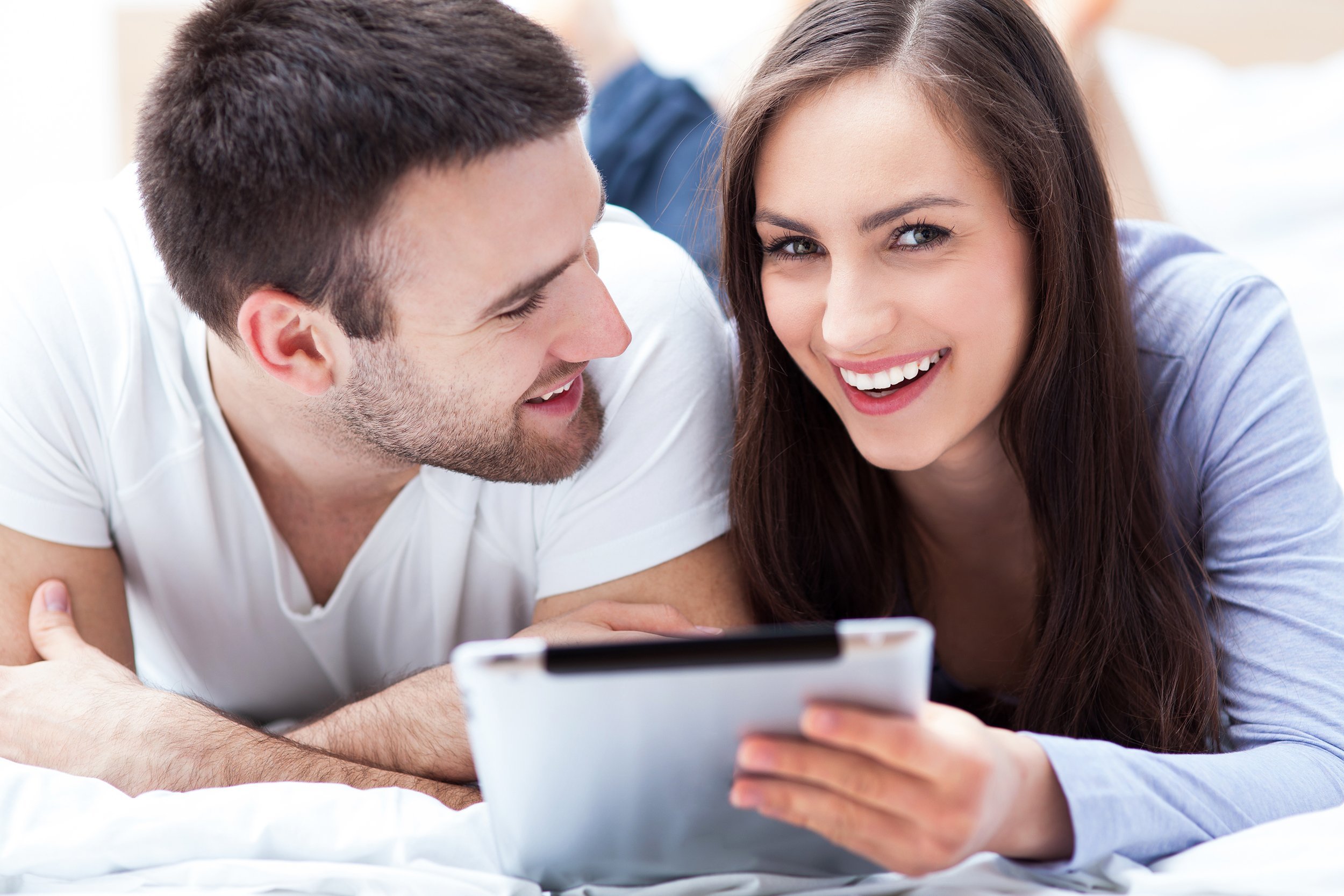 smiling couple with digital tablet lying on bed