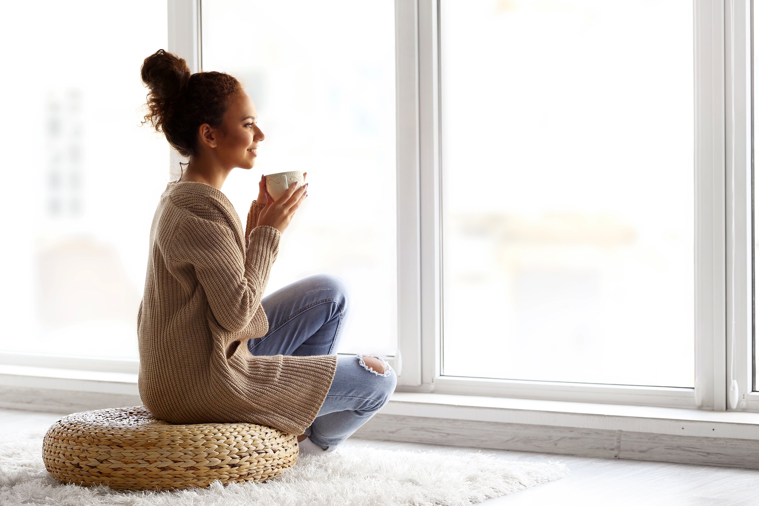 Young woman having coffee in front of a large window at home