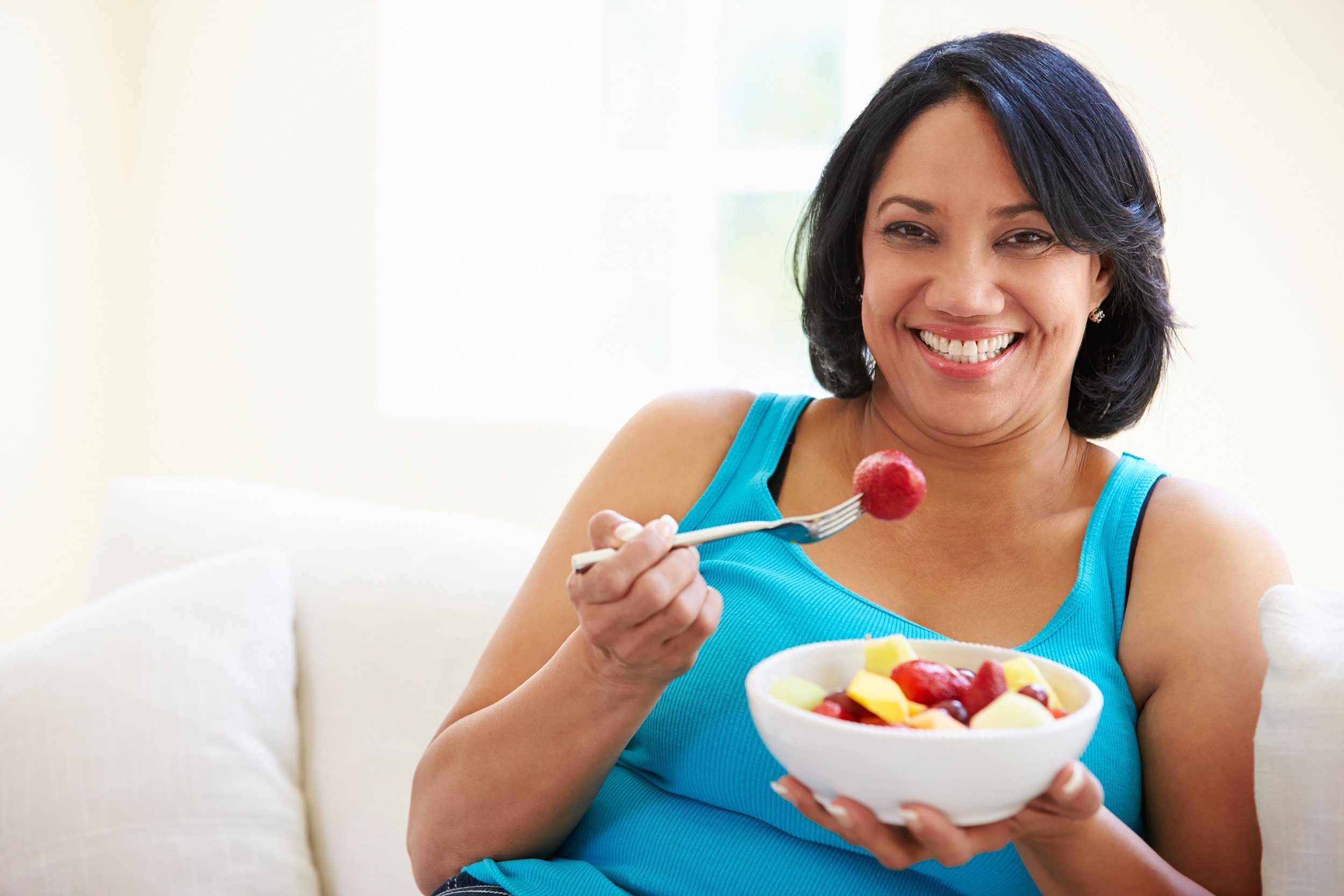 African American woman eating a bowl of fruit on the couch