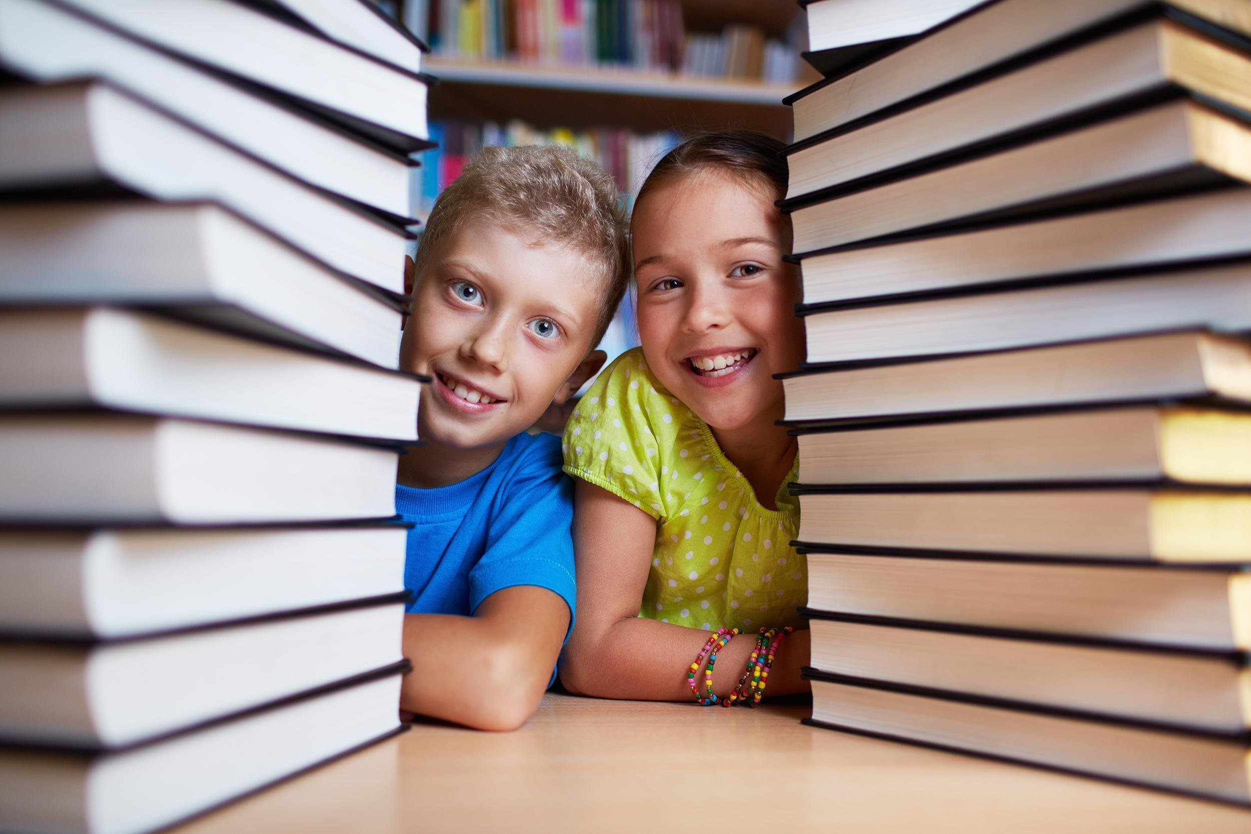happy schoolkids between stacks of books looking at camera