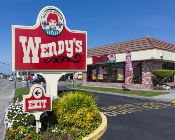Sign and exit sign of Wendy's fast food restaurant, Seaside, California with drive-thru road and restaurant building in the background, at an intersection, against a clear blue sky