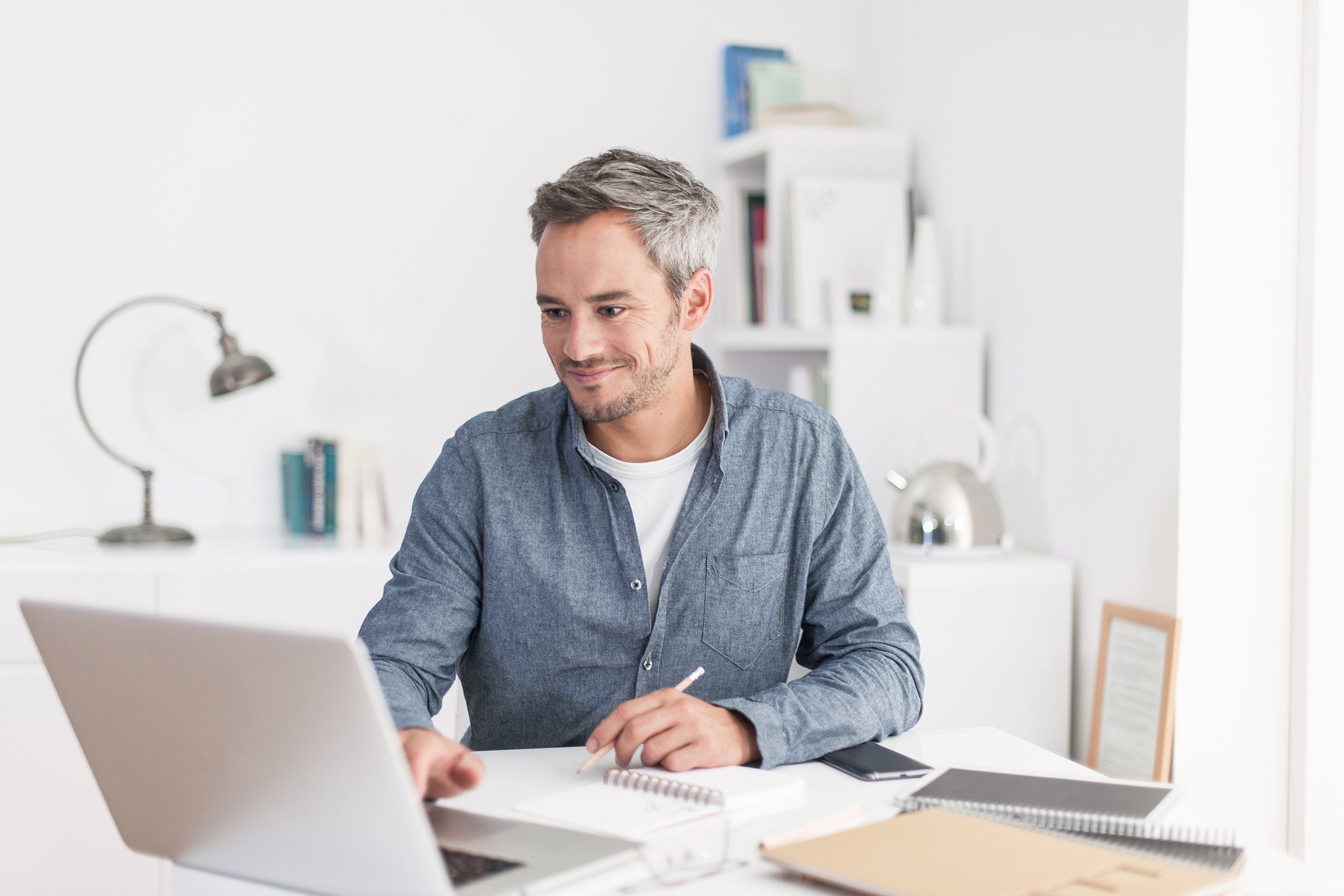 smiling grey hair man with beard working on laptop in home office