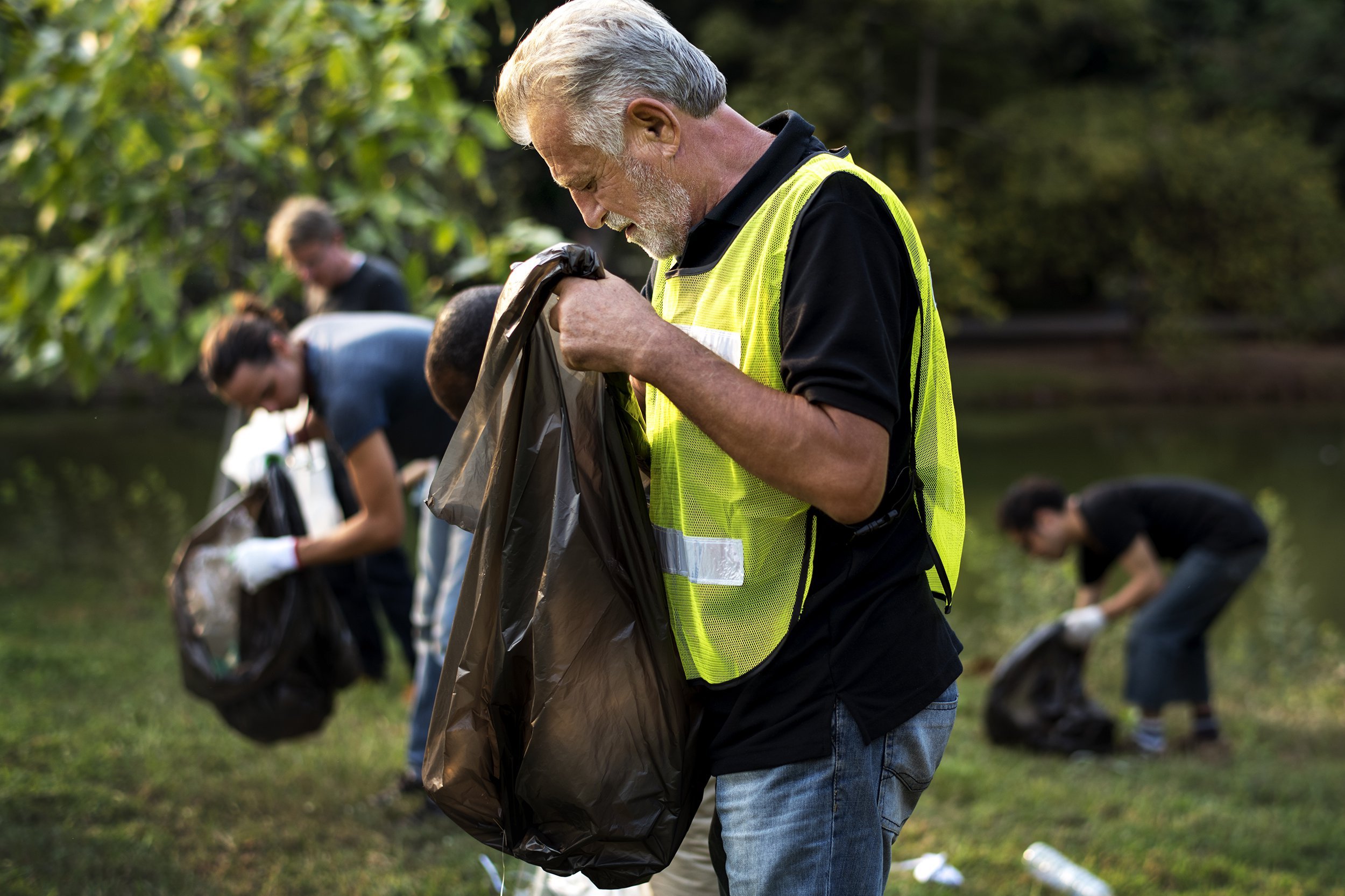 senior man cleaning up park with volunteer group