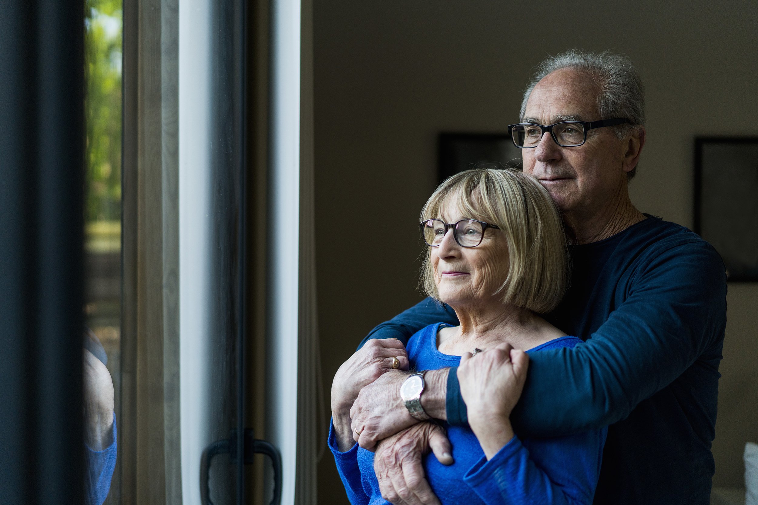 thoughtful senior couple looking through window