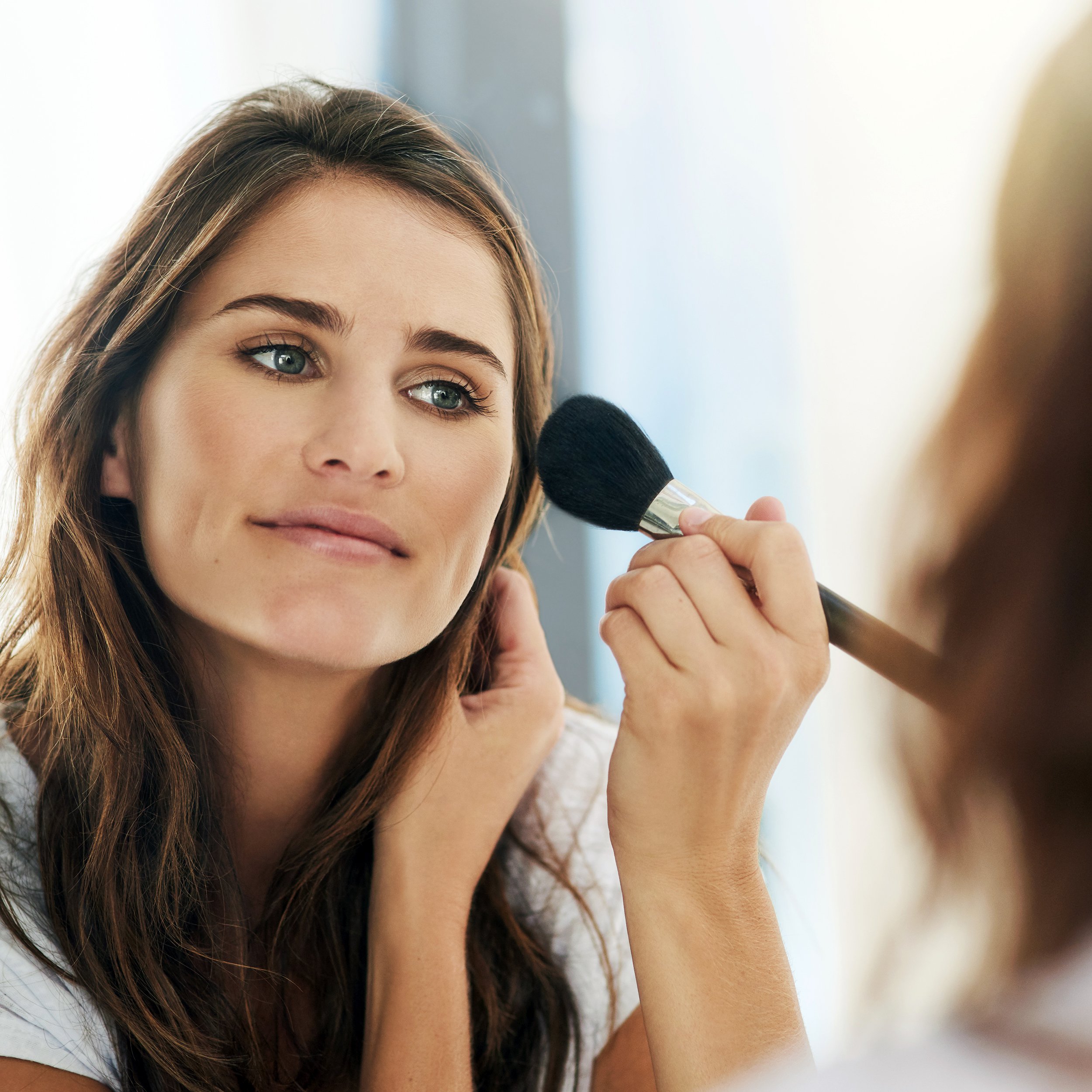 woman looking in mirror, blending her makeup for a natural look