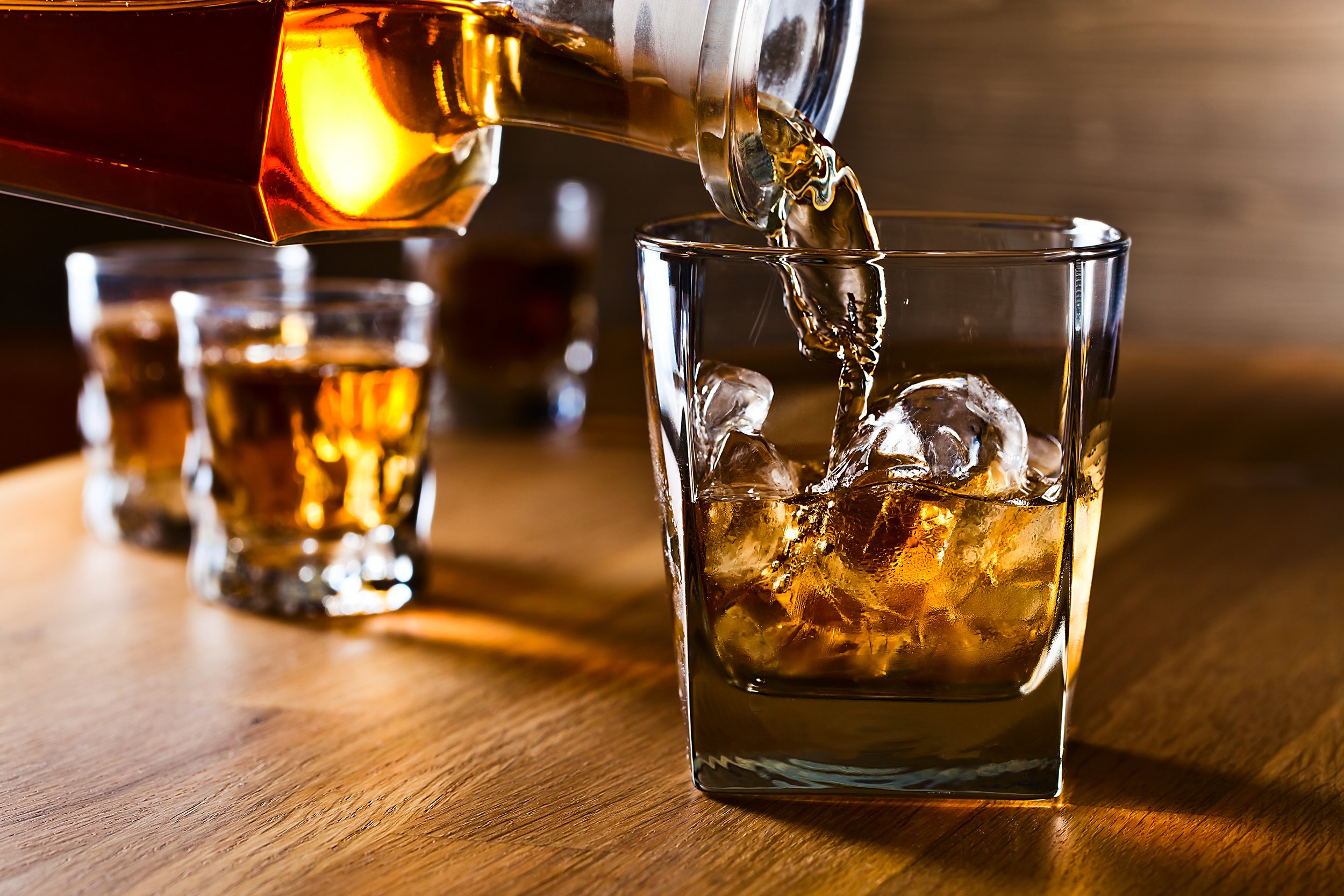 bottle pouring into a glass of whiskey with ice