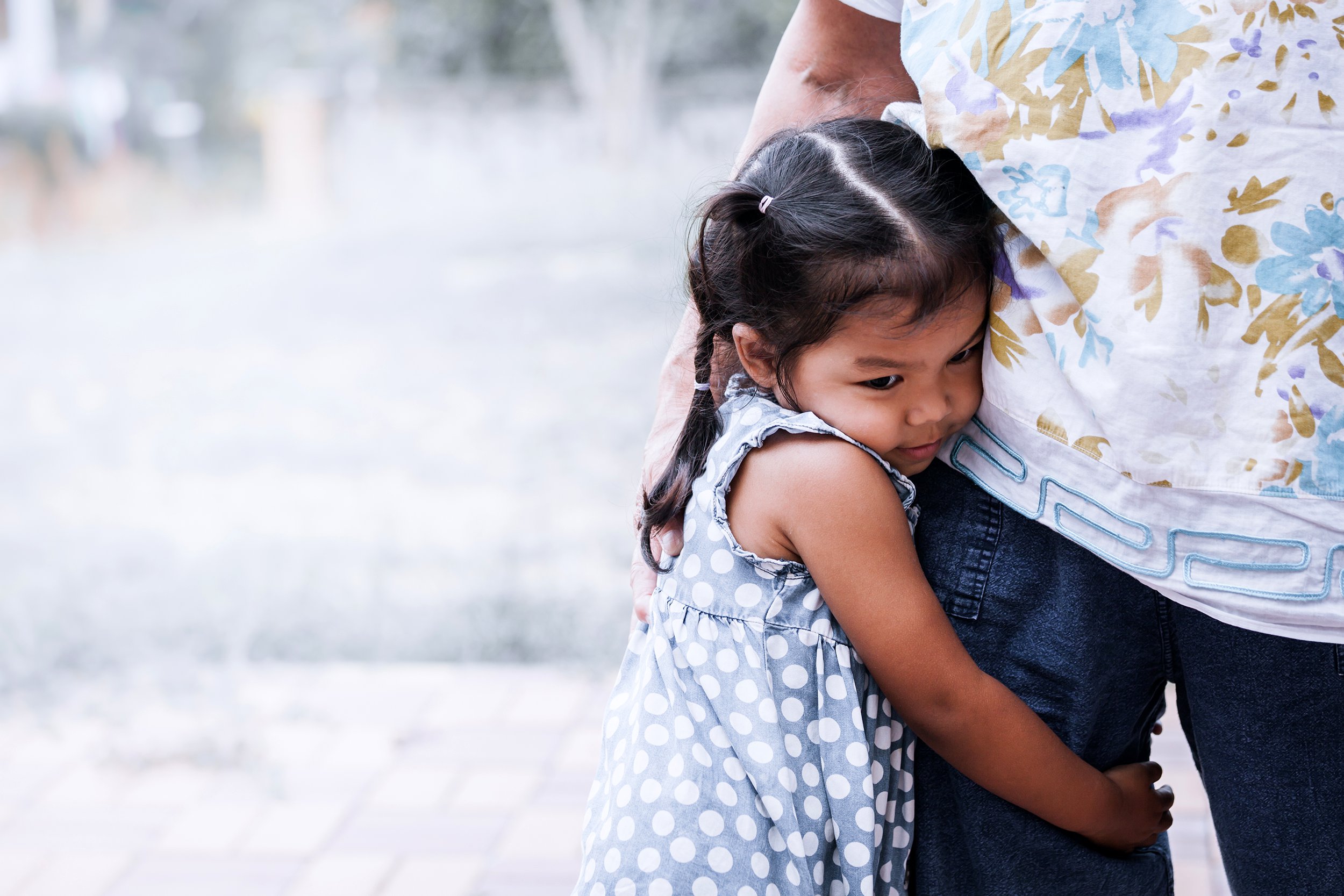Young girl looking sad and hugging her mother's leg