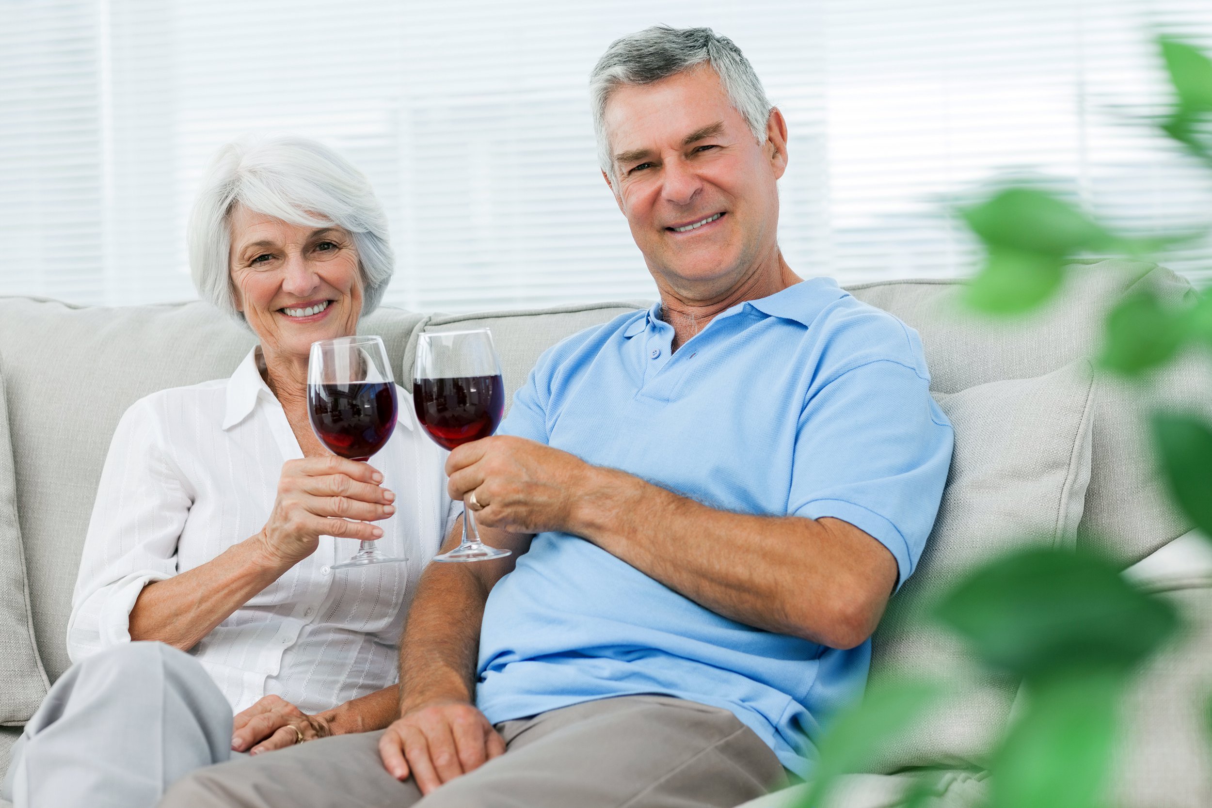 Old couple sitting on the couch having a glass of red wine