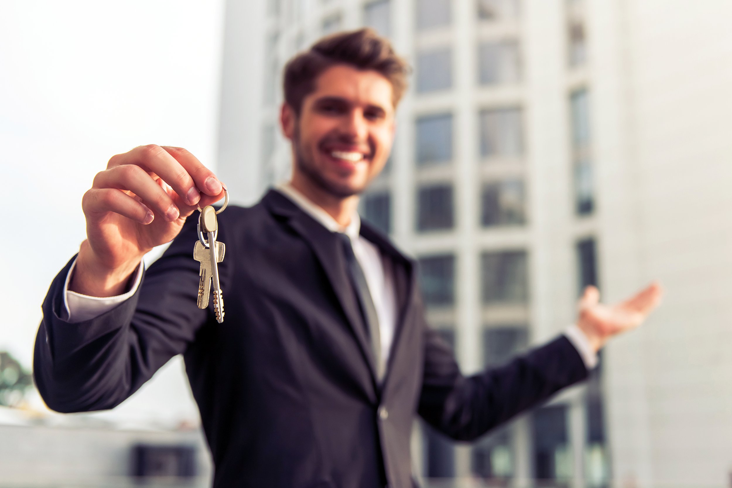 Real estate agent holding keys out and standing in front of a building