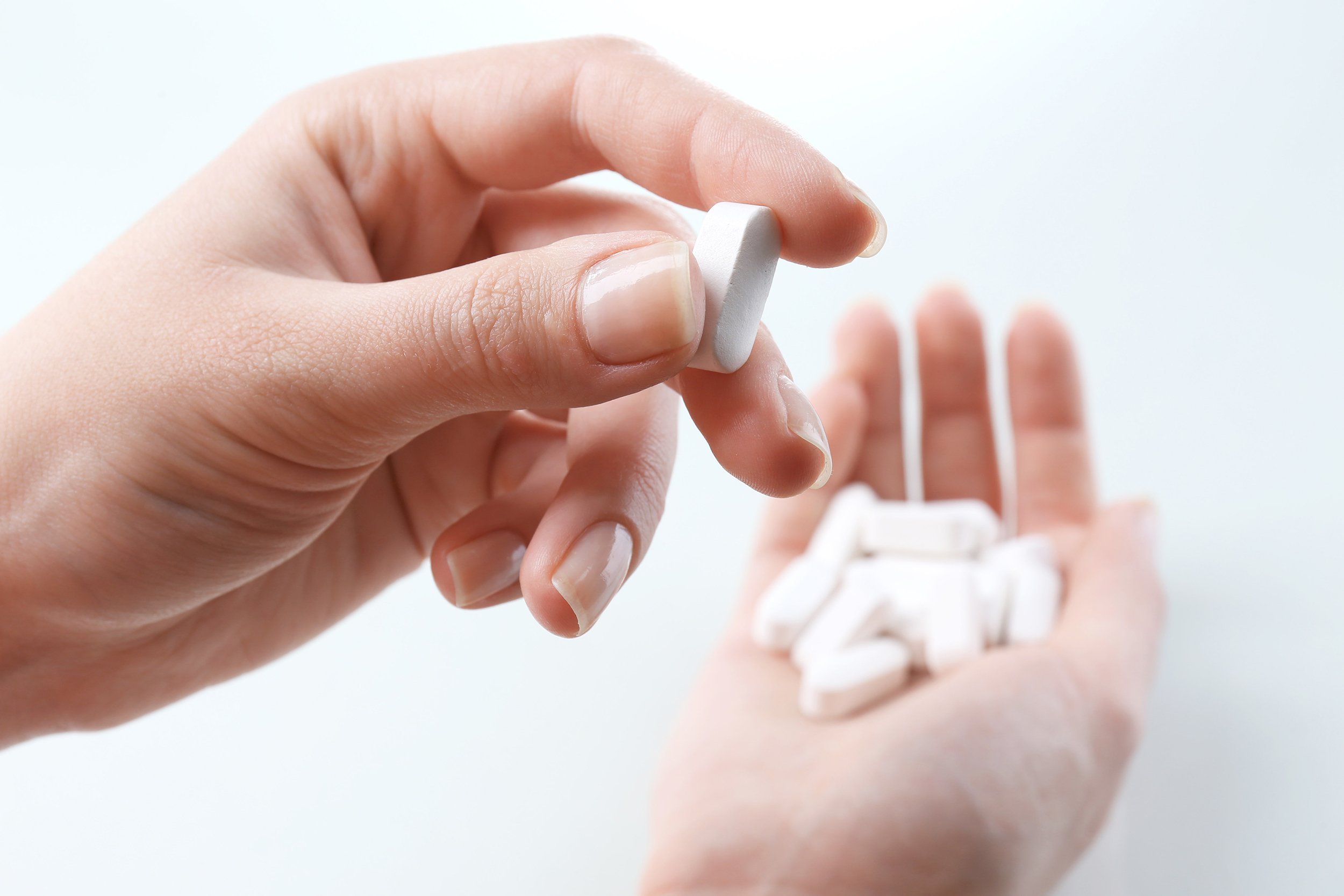 calcium pills in hand with close up of a pile in left hand