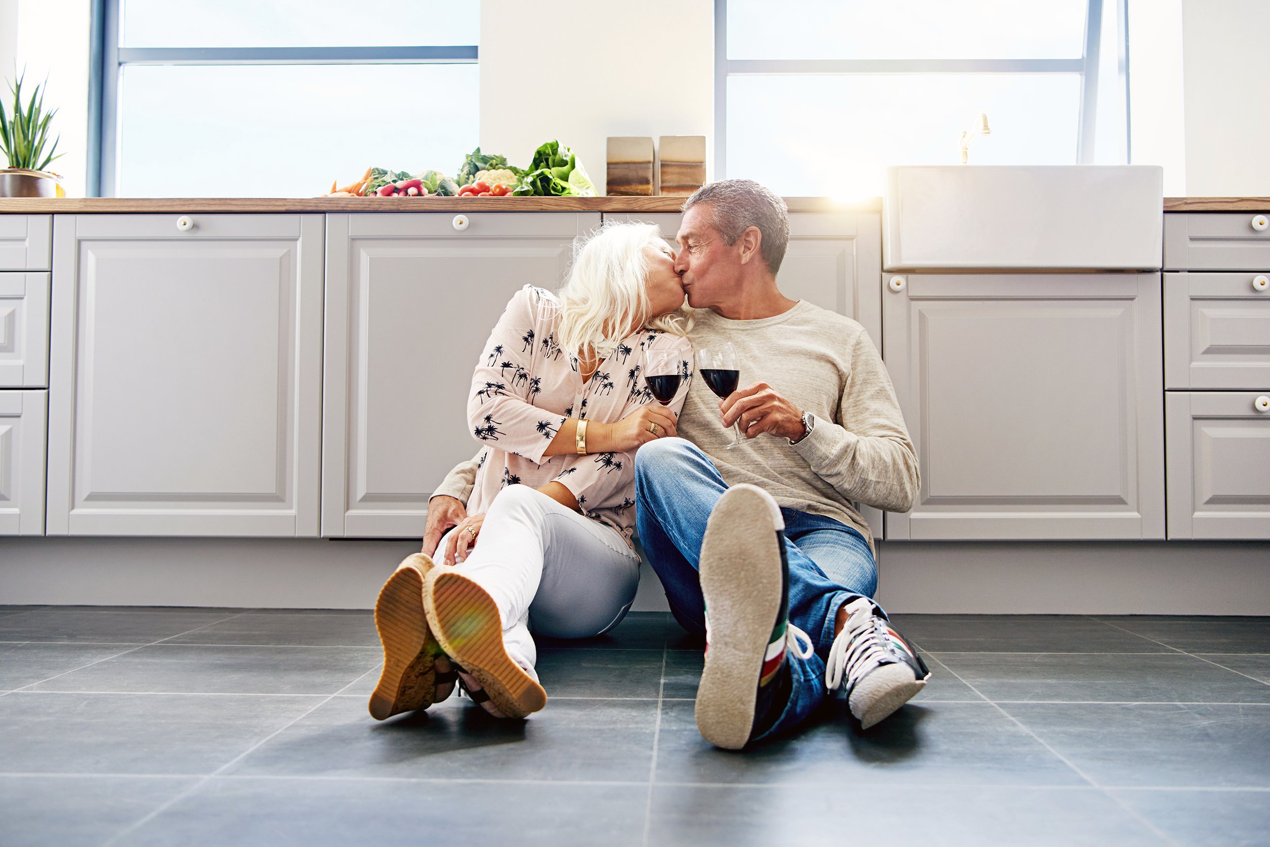Senior couple sitting on the floor of the kitchen drinking wine together