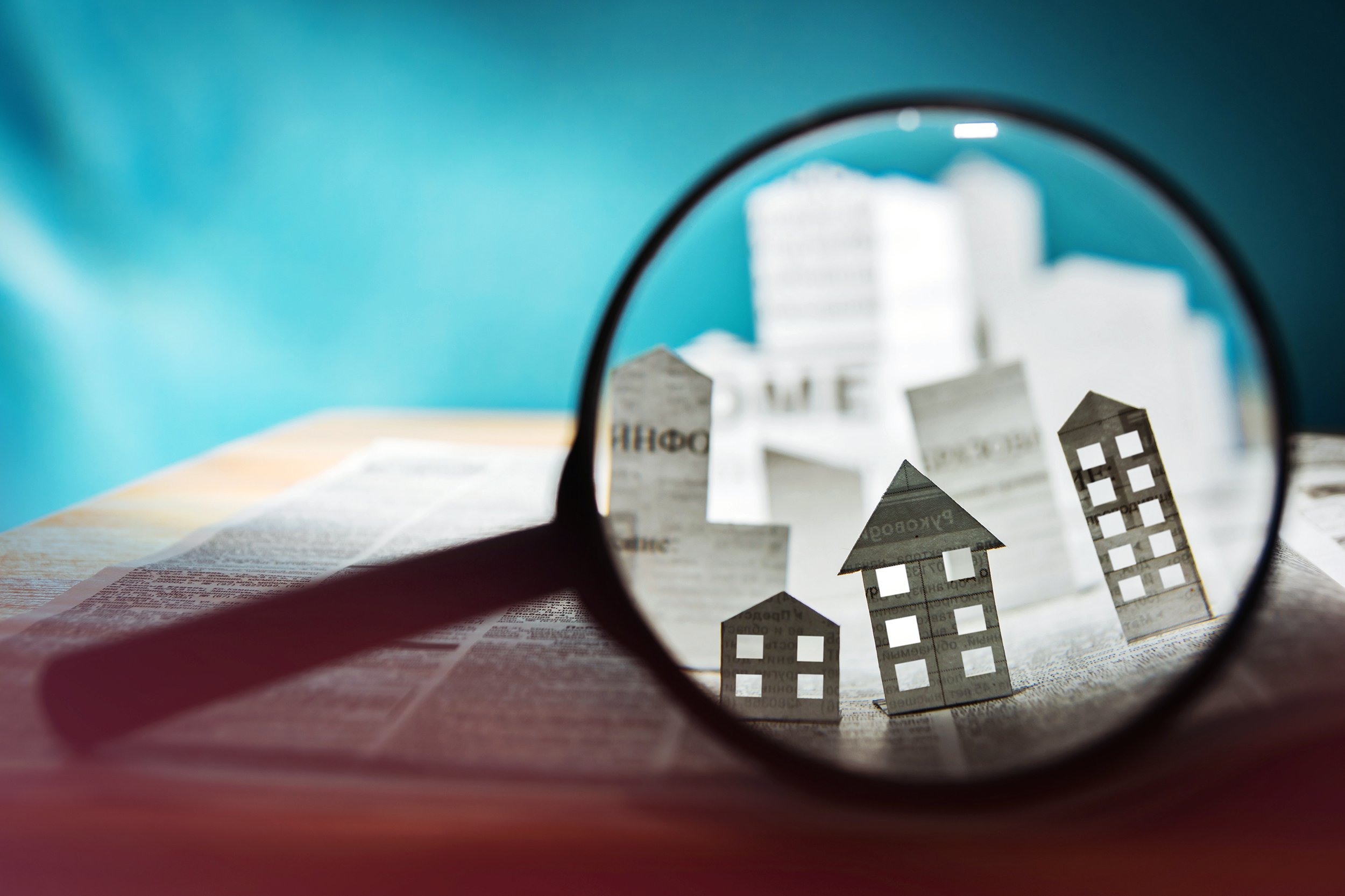 Magnifying glass looking at paper houses and condo buildings