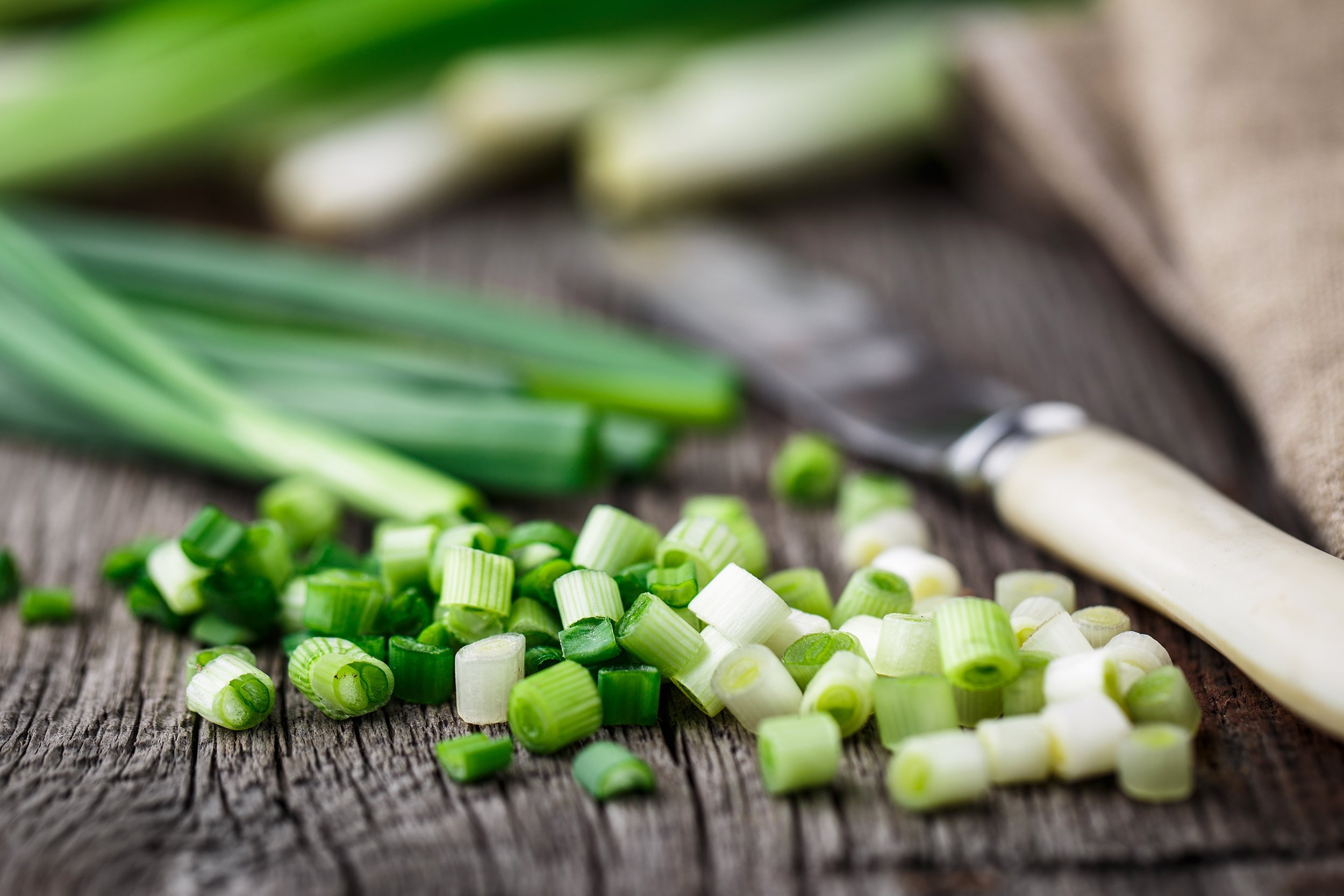chopped scallions with knife on wooden table