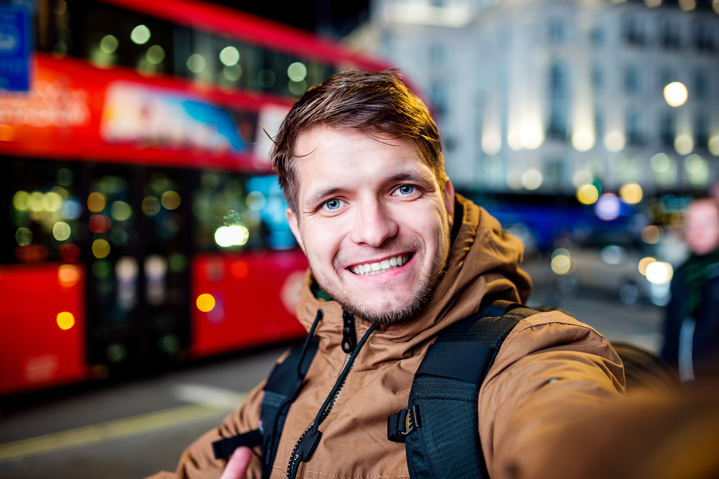 Man taking a selfie in front of red double-decker bus in London at night