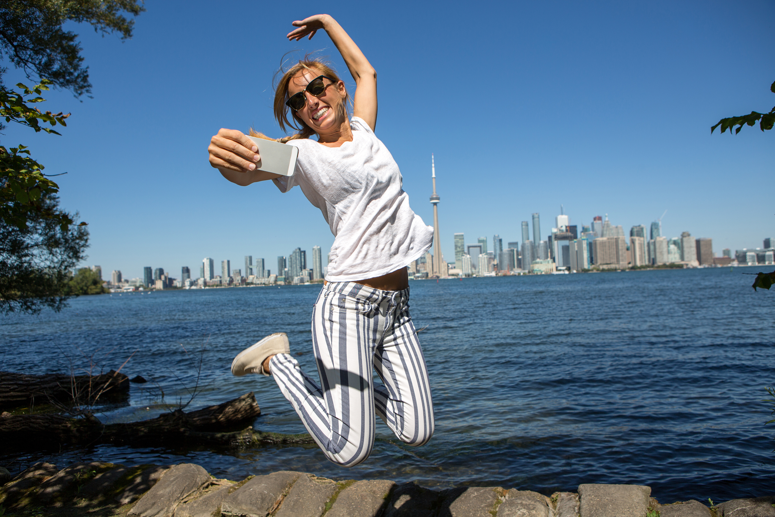 Woman jumping and taking a selfie in front of city skyline