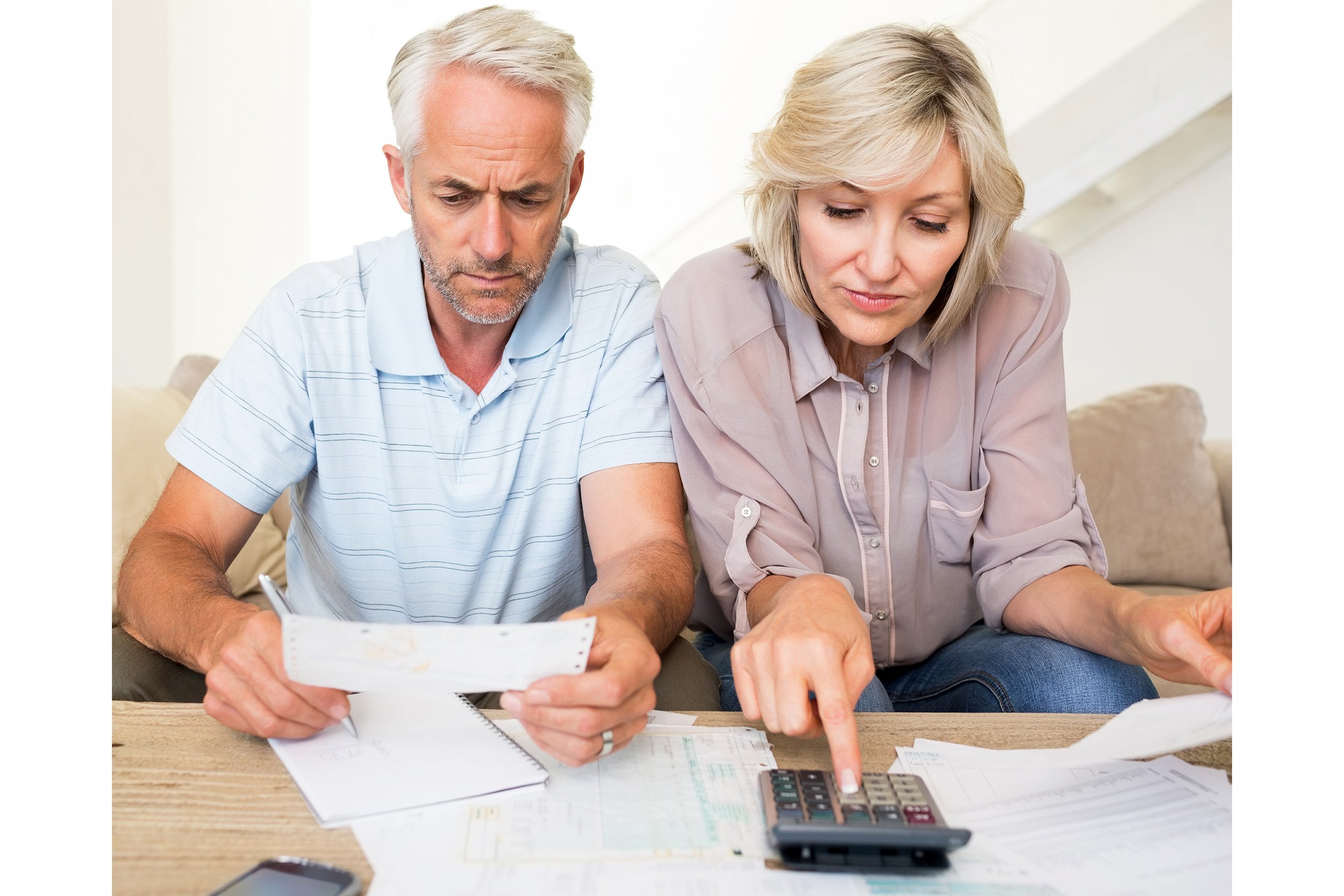 Concentrated mature man and woman with bills and calculator sitting on sofa at home