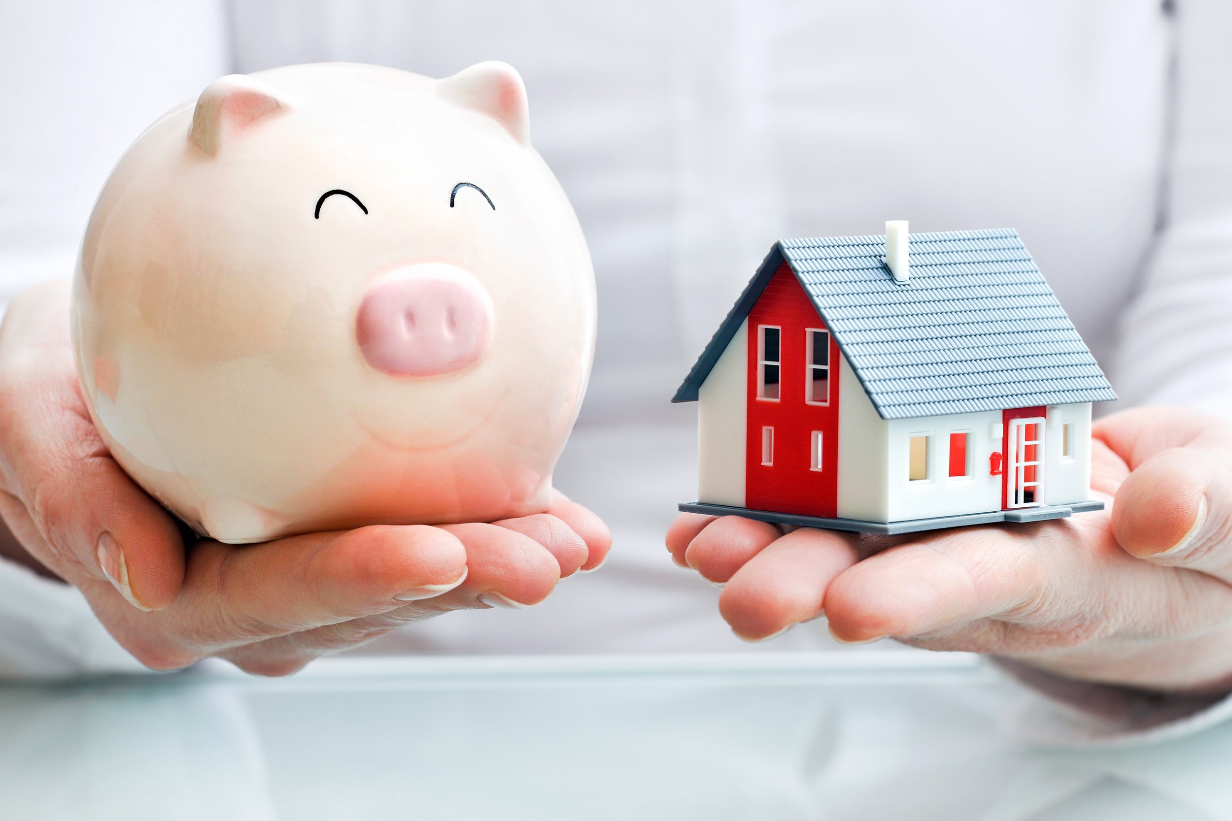Hands holding a small model home and a piggy bank