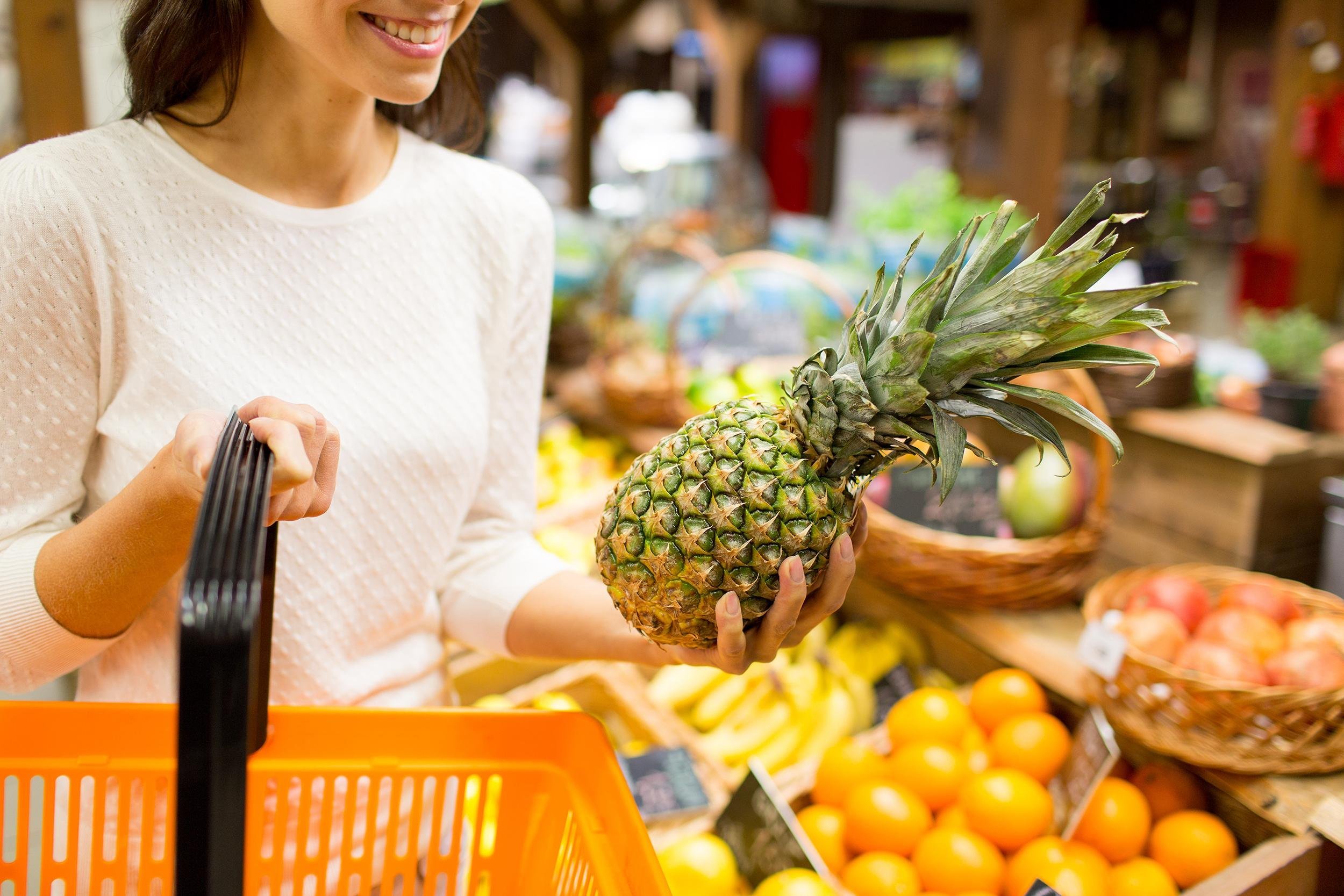 close up of woman with food basket and pineapple in grocery market