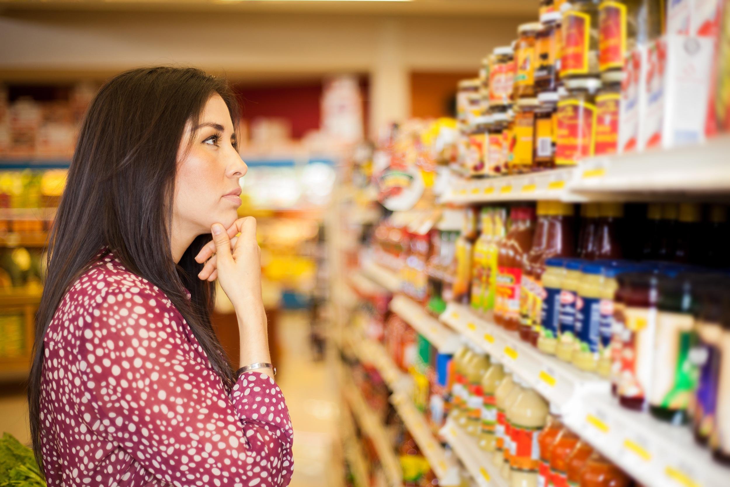 woman looking at some shelves in a supermarket trying to decide what to buy