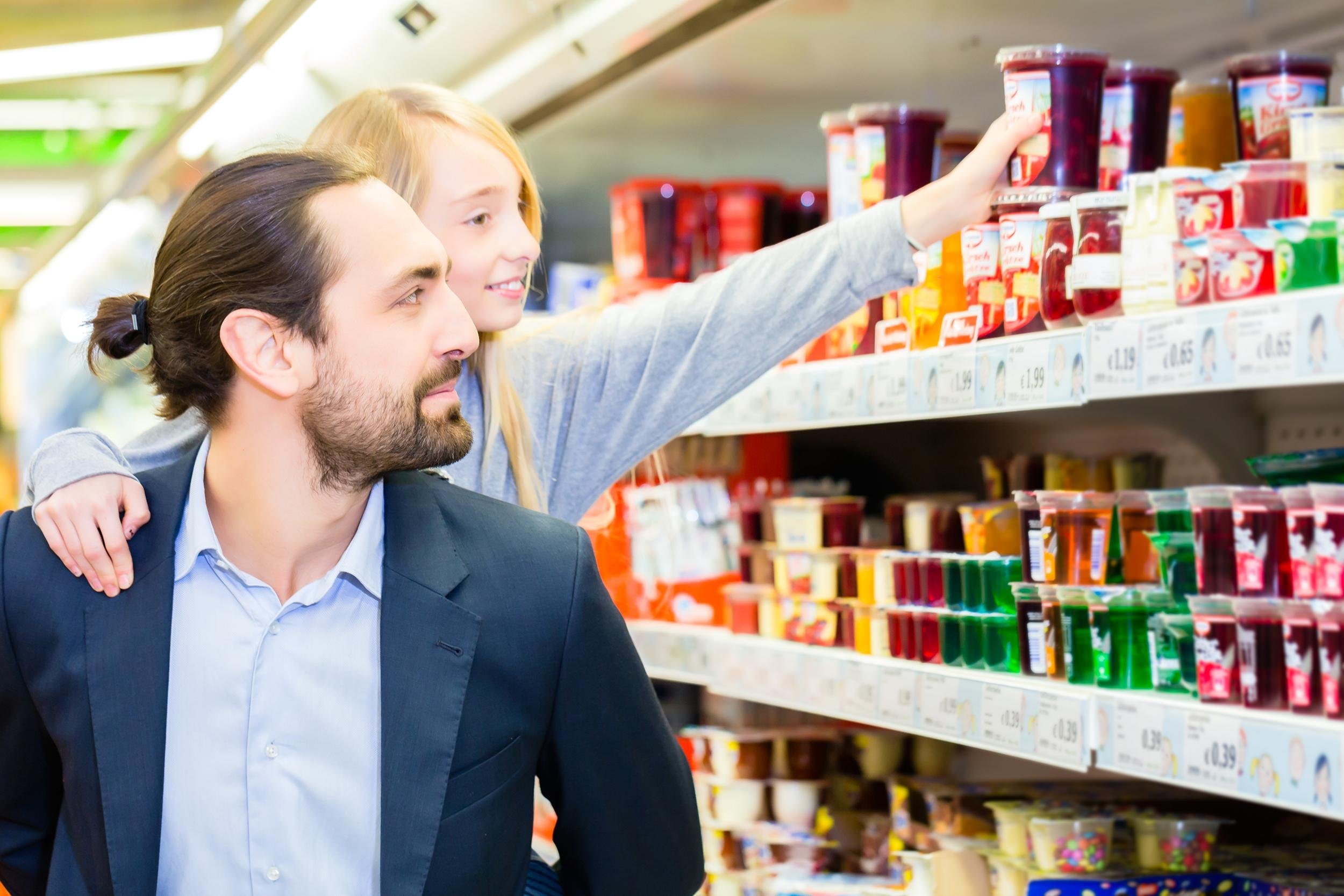 father carrying daughter on his back while she is selecting dessert at grocery shopping in supermarket