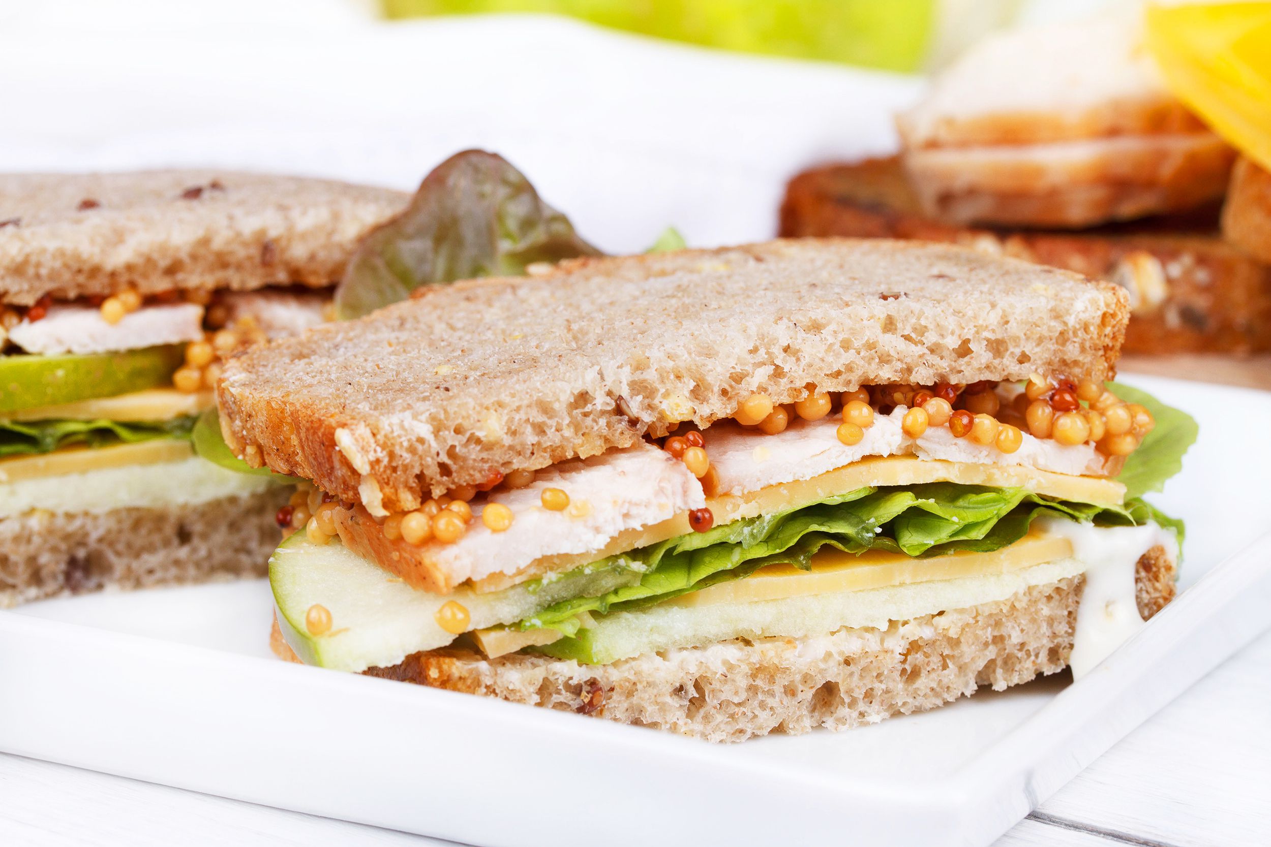 Cheddar apple sandwich cut in half, lined behind one another on a white rectangle porcelain plate, selective focus, white tablecloth and bread blurred in the background